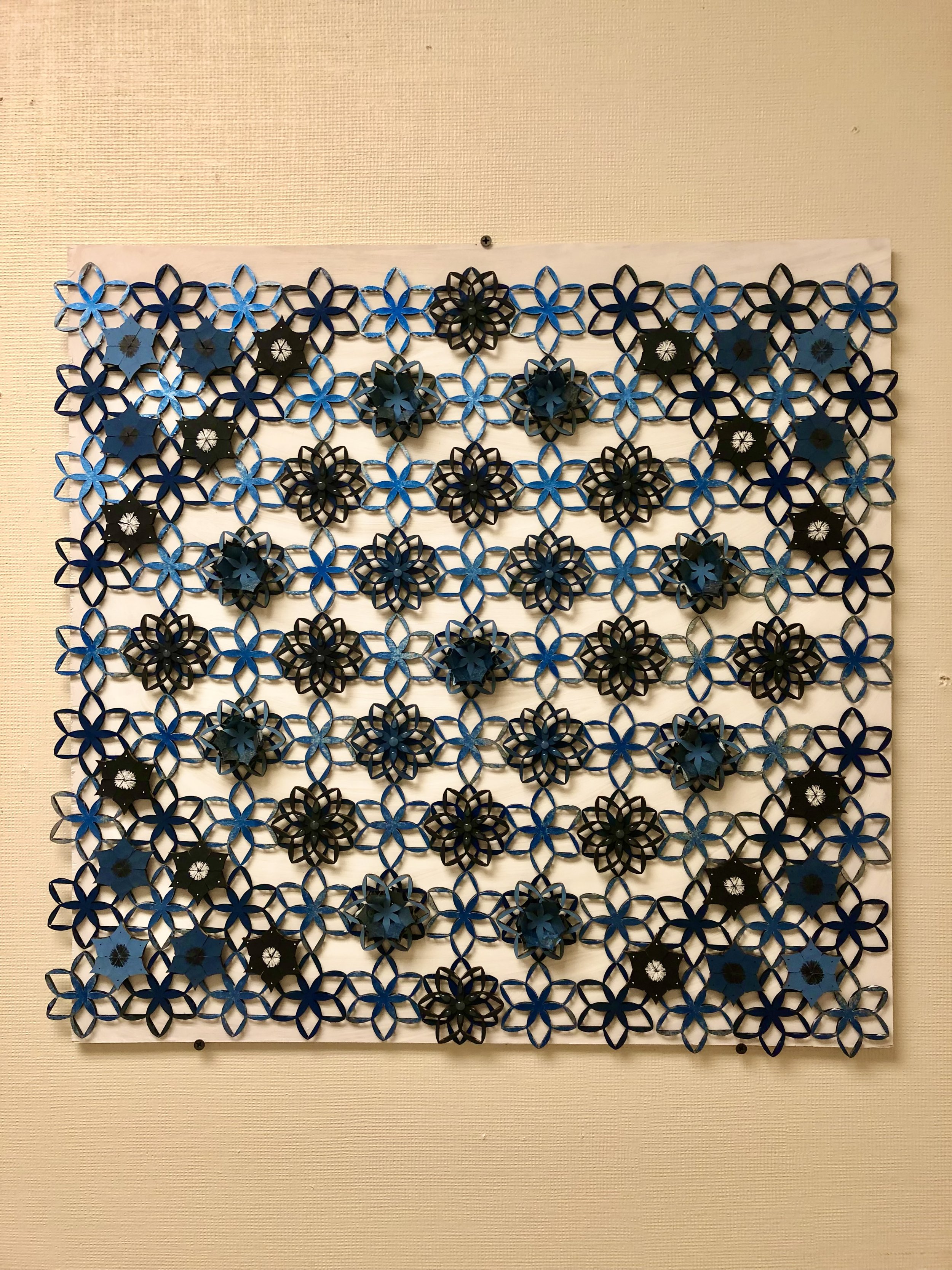 A tessellation made from cardboard, spray painted, and attached to plywood.