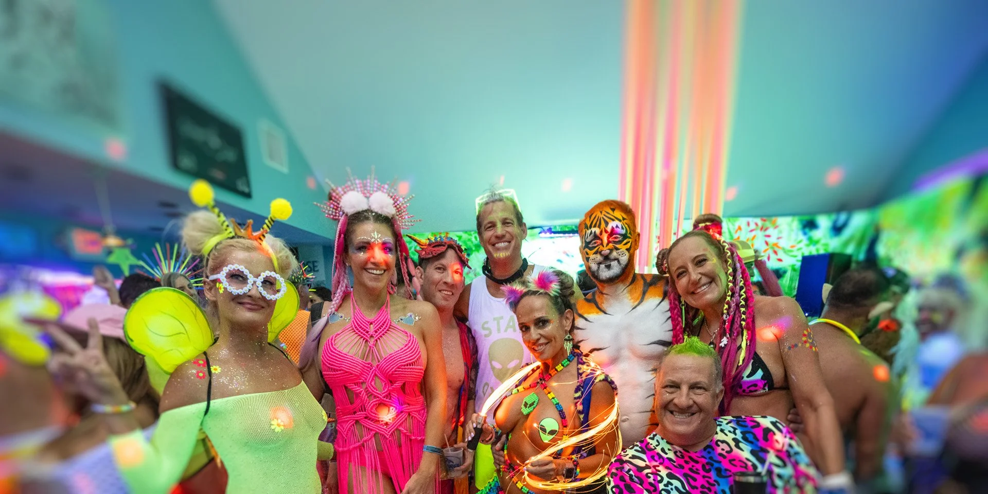 Group of people in neon and colorful costumes at a party with glowing decorations in a vibrant, lively setting.