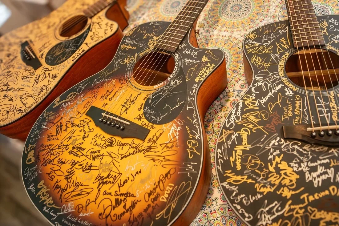 Three signed acoustic guitars on a table with a colorful, patterned tablecloth.