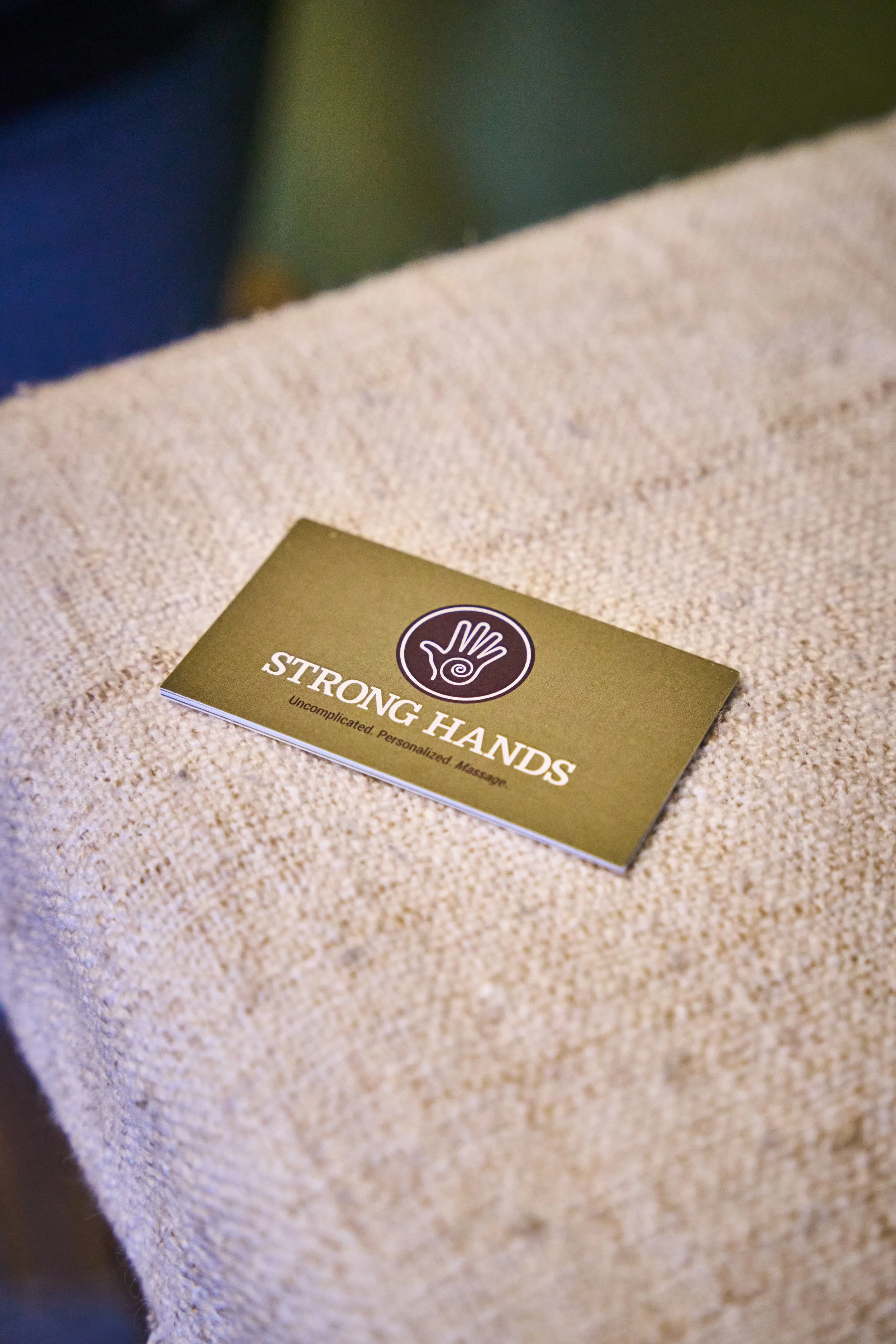 Business card that reads 'Strong Hands' with a logo of a hand with a spiral in the palm, placed on a textured beige surface.