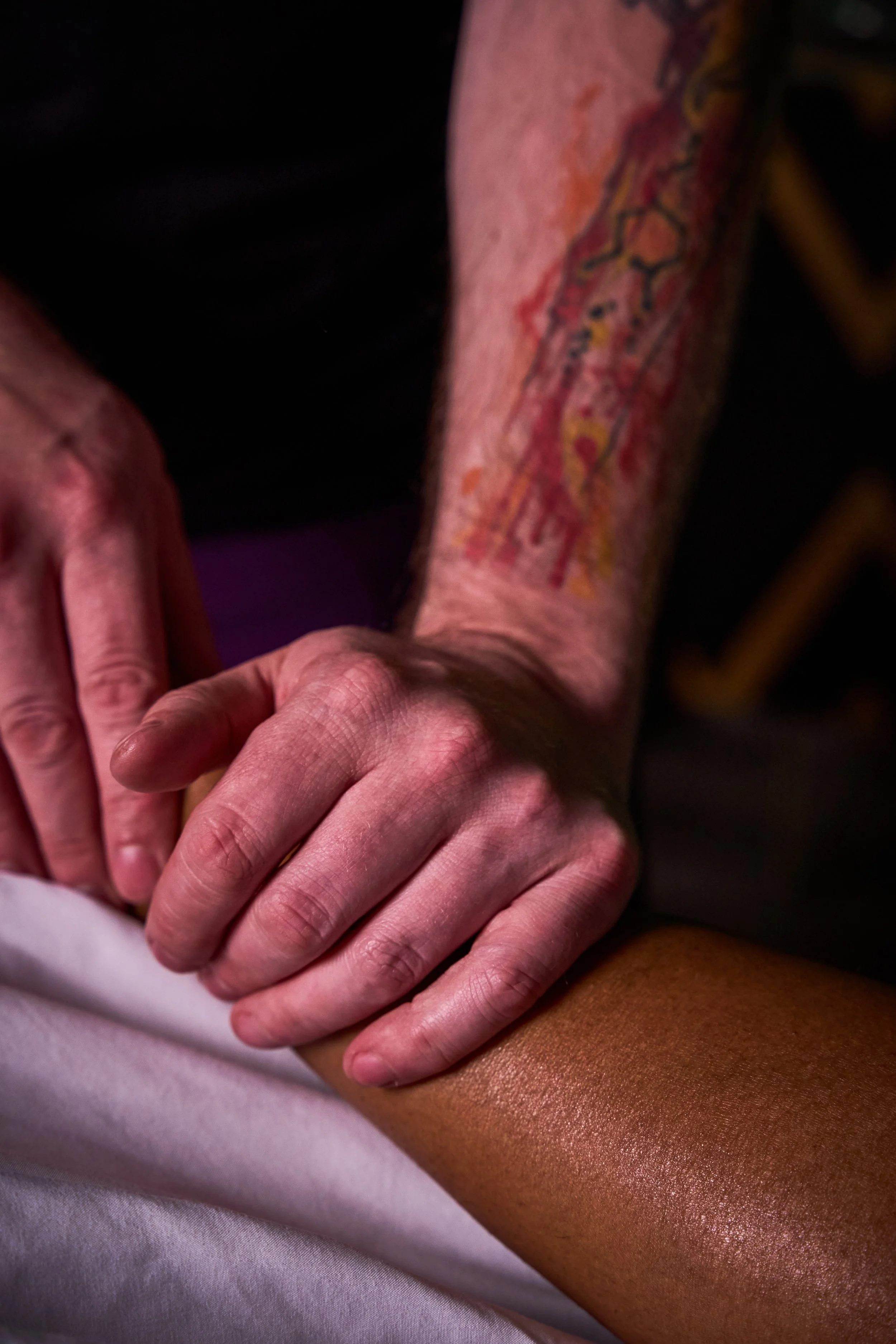 Close-up of a person's tattooed arm and hand resting on another person's arm.