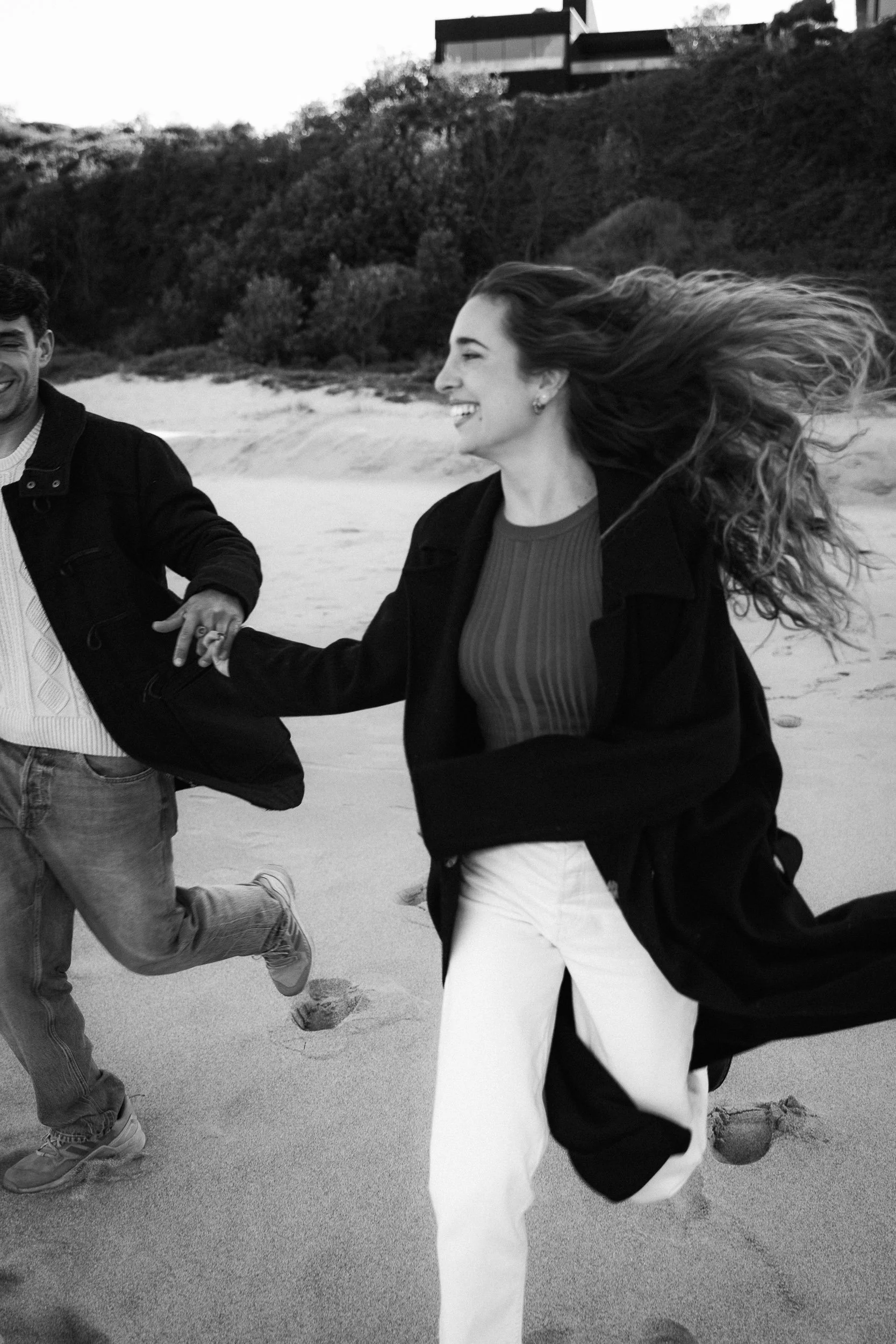 A joyful couple running hand in hand on the beach during their engagement session in Sydney, capturing a fun moment together.