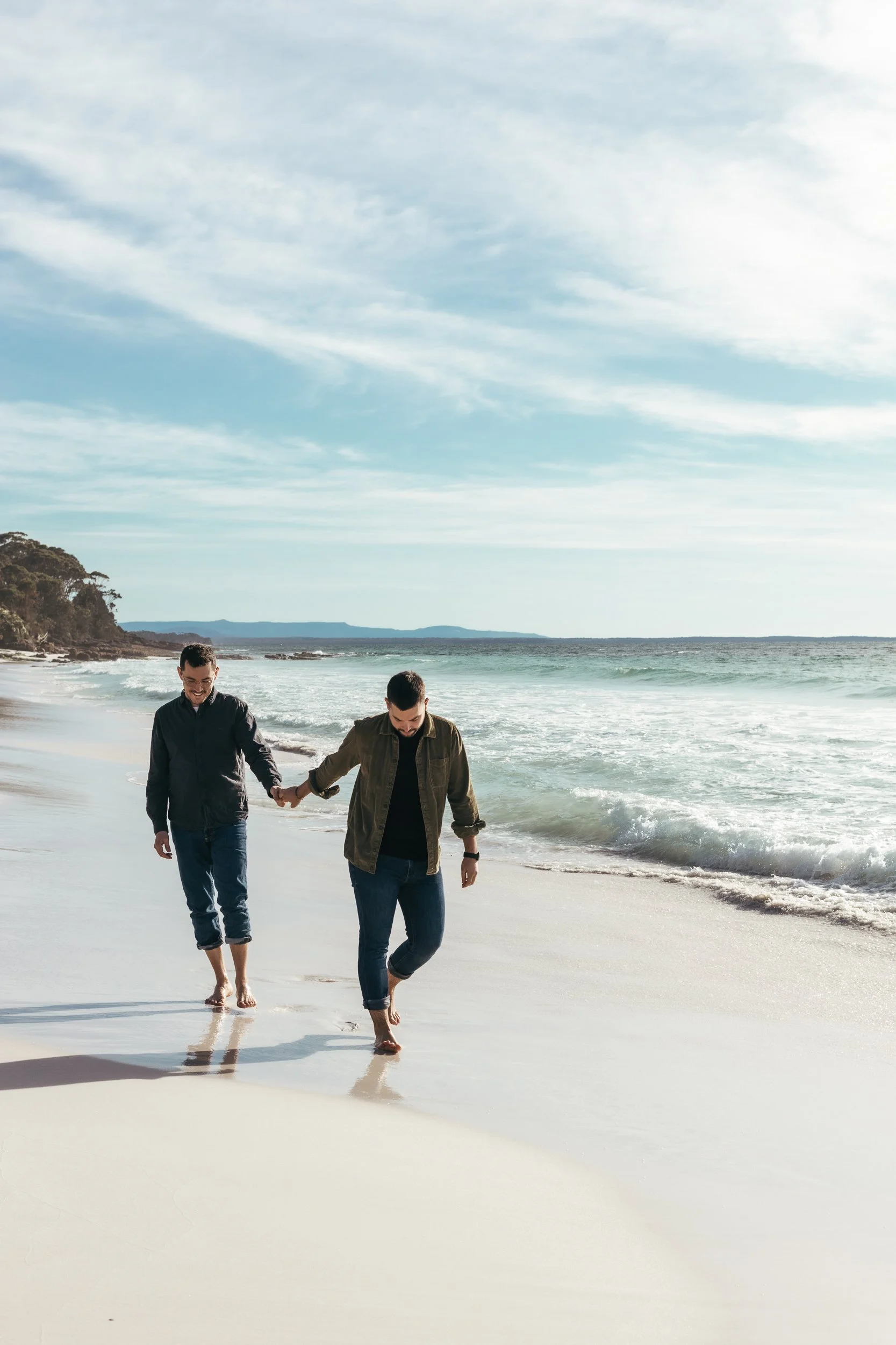 Two men stroll along the beach, hand in hand, celebrating their love in a fun couple's photo shoot in Sydney.
