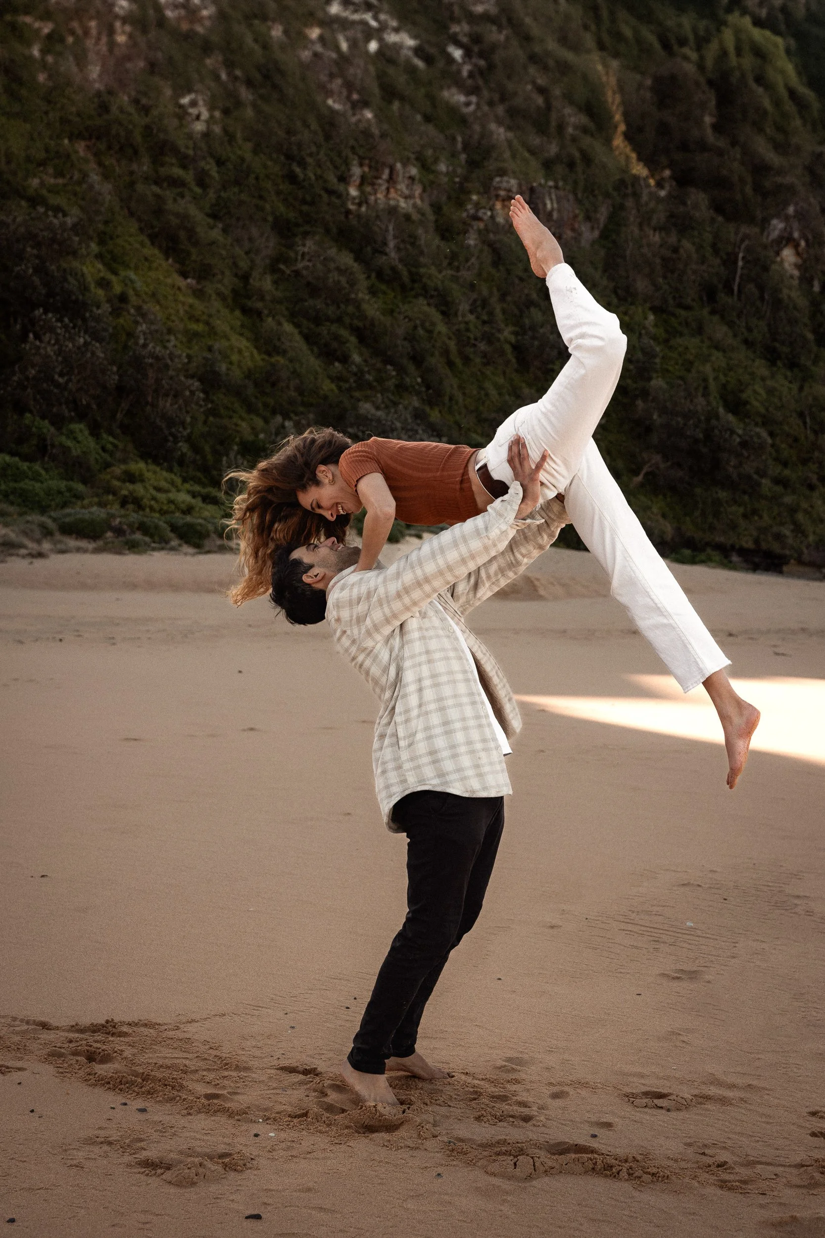 A man and woman mid-flip on a beach, embodying fun and artistry in a couple's photography shoot in Sydney.