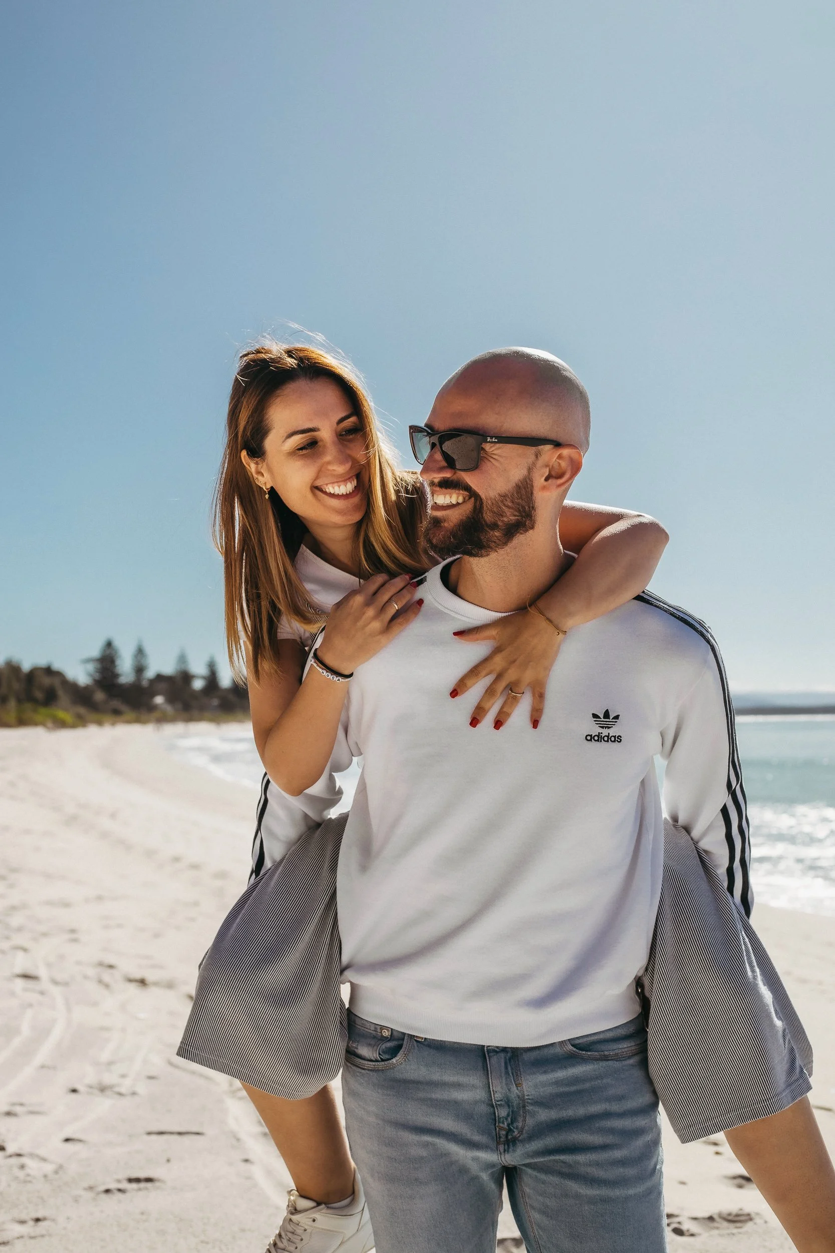A couple enjoys a playful moment at the beach, with a man lifting a woman on his shoulders, showcasing their fun in the beach