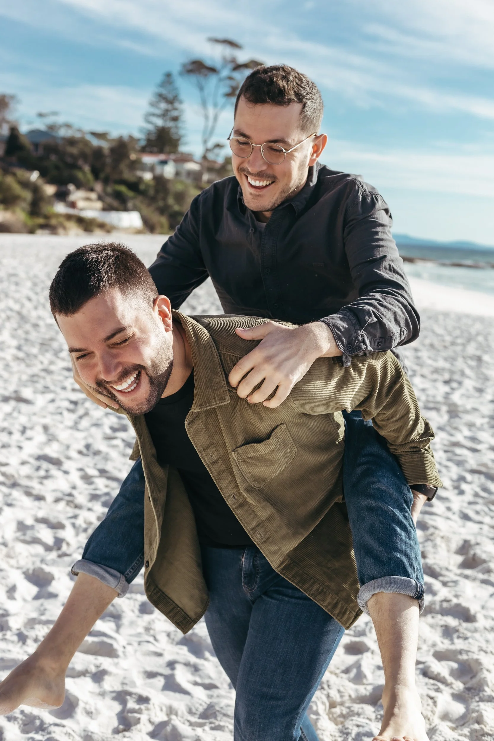 A happy gay couple holds each other on the beach, showcasing their love in a vibrant Sydney beach