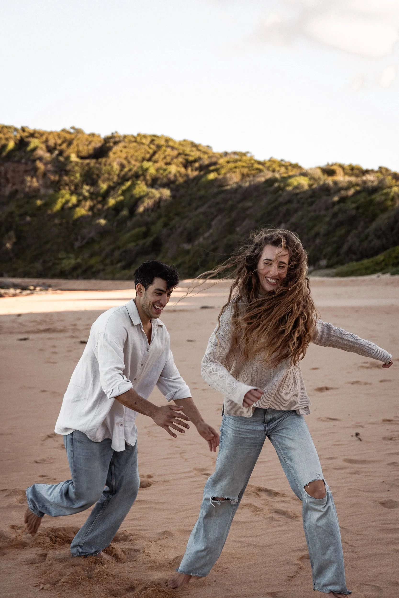 A man and woman run playfully along the beach, photographed in Sydney, highlighting their fun and energetic connection.