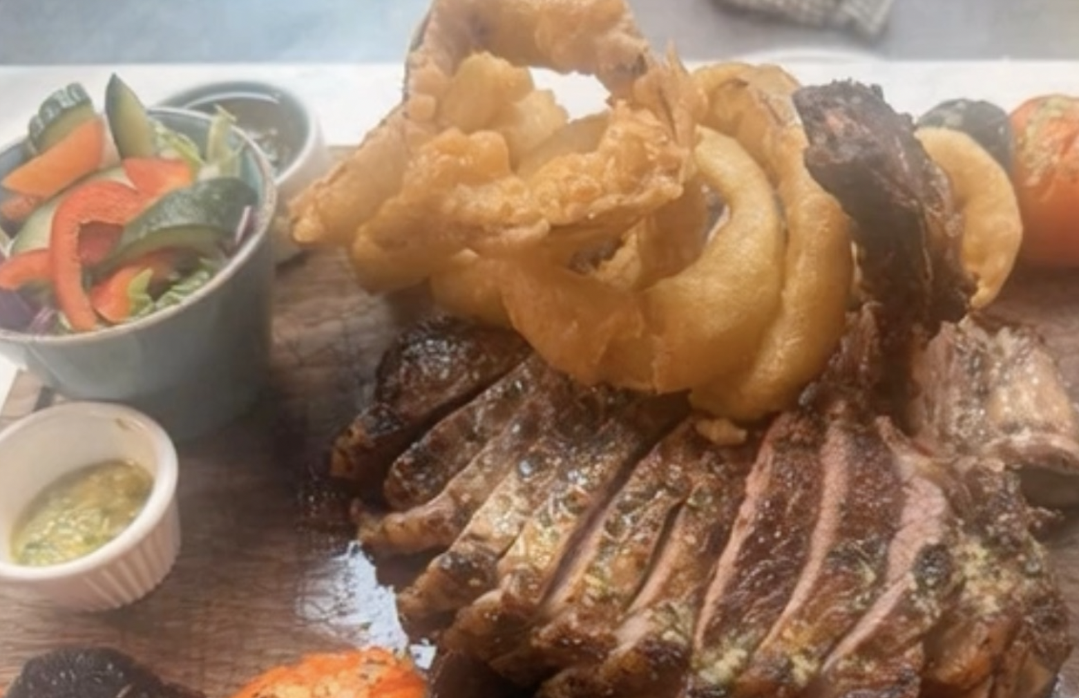 A platter of grilled steak topped with fried onion rings, served with side salads and dipping sauces.