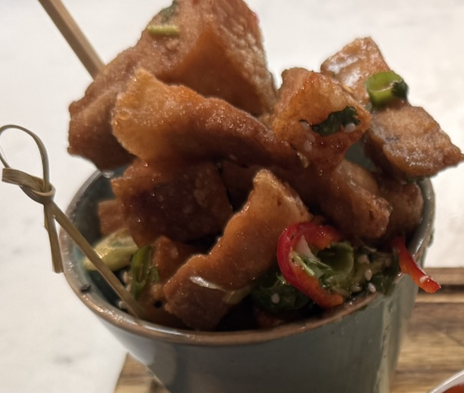 Close-up of crispy fried paneer cubes garnished with sliced green chilies and red chilies in a small metal serving vessel.