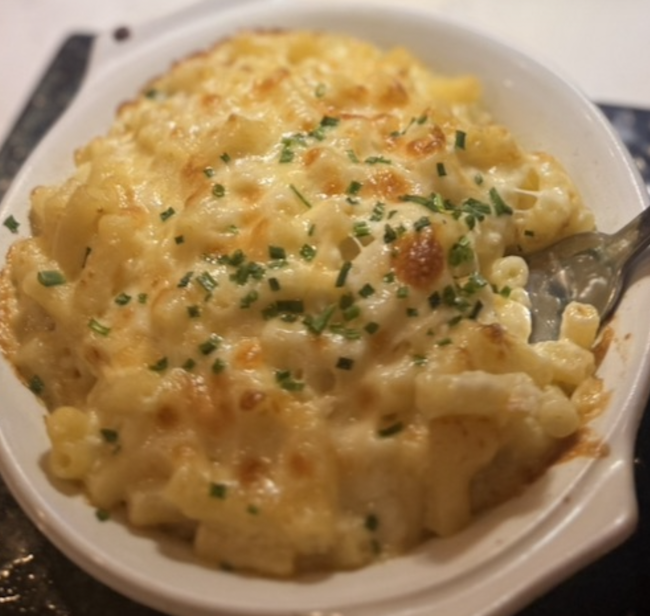Baked macaroni and cheese topped with chopped green herbs in a white dish with a spoon.