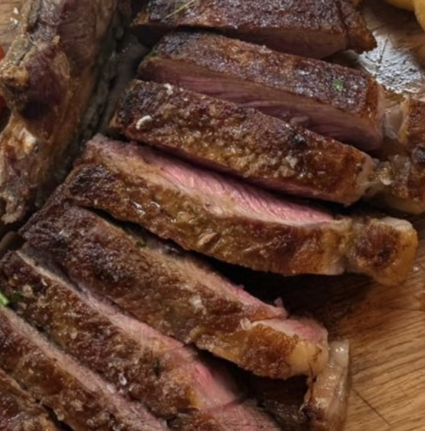 Sliced medium-rare steak on a wooden cutting board.