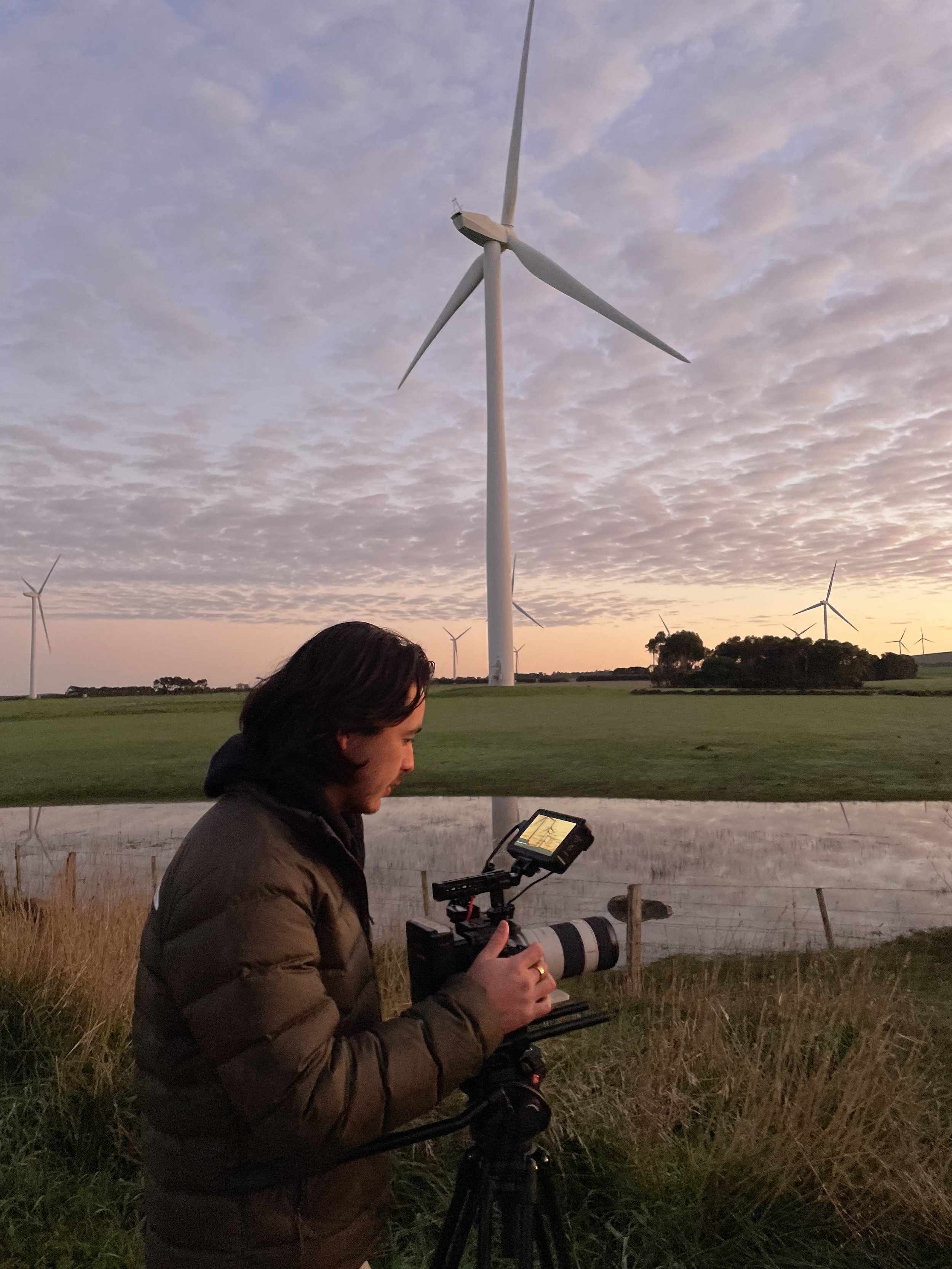 Person with camera filming near wind turbines at sunset