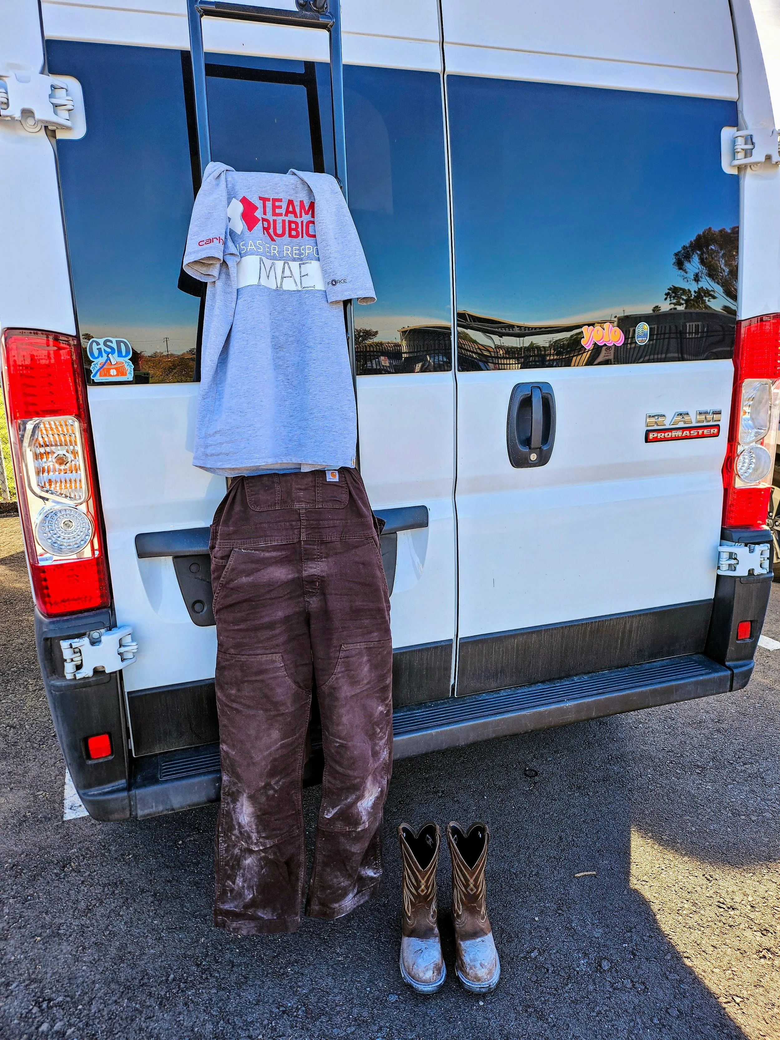 A team member's clothing and boots displayed against the back of Mae's van, ready for the road