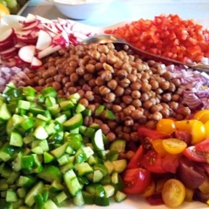 Chopped vegetables and chickpeas, including radishes, red bell peppers, cucumbers, cherry tomatoes, and red onions, arranged on a platter.