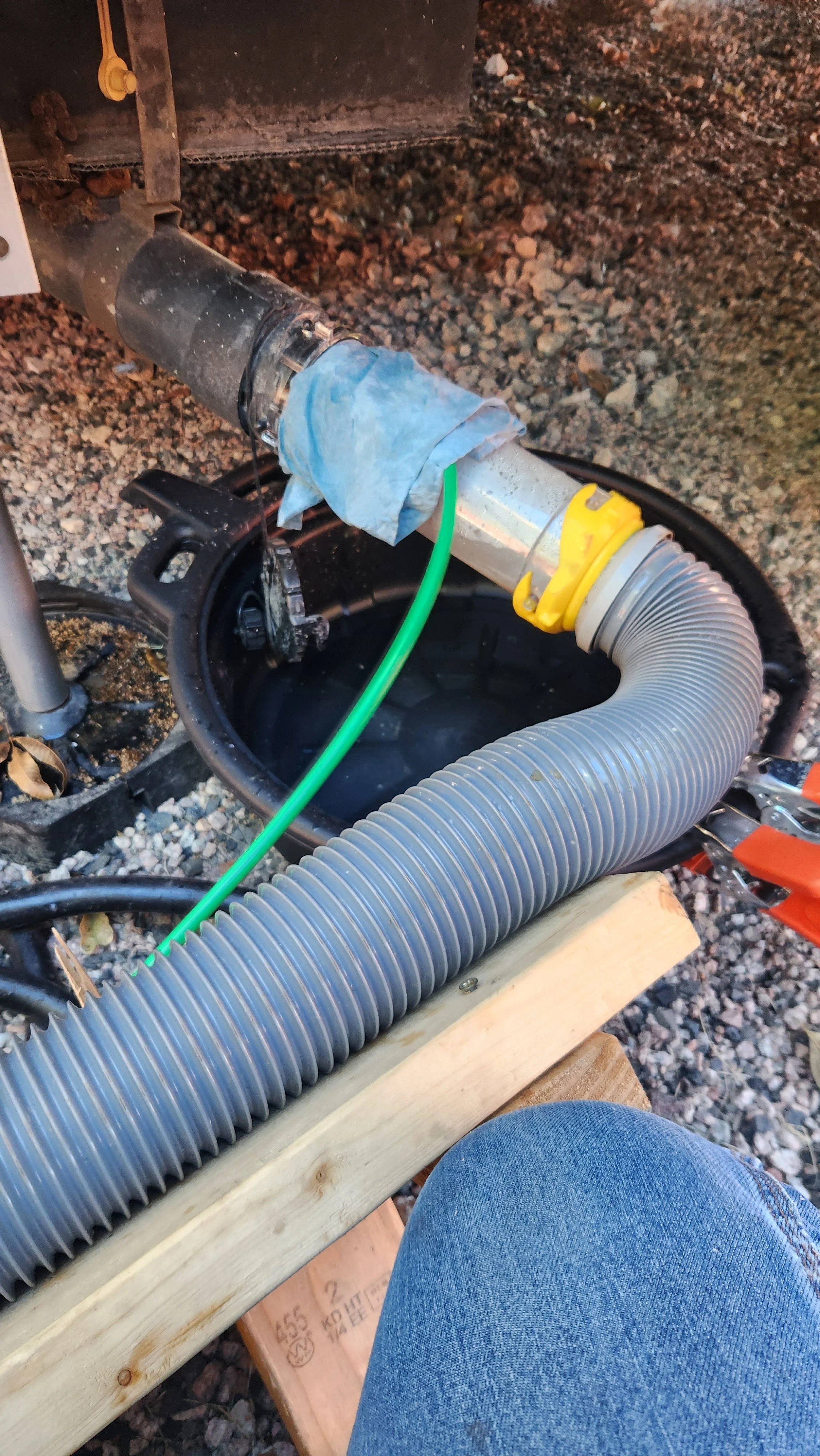 Outdoor plumbing with hoses and pipes, likely part of a construction or repair setup, with a person wearing jeans nearby.