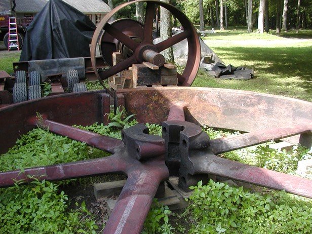 Here, next to the crankshaft, the two halves of the flywheel lie in the weeds none the worse for their outdoor storage.