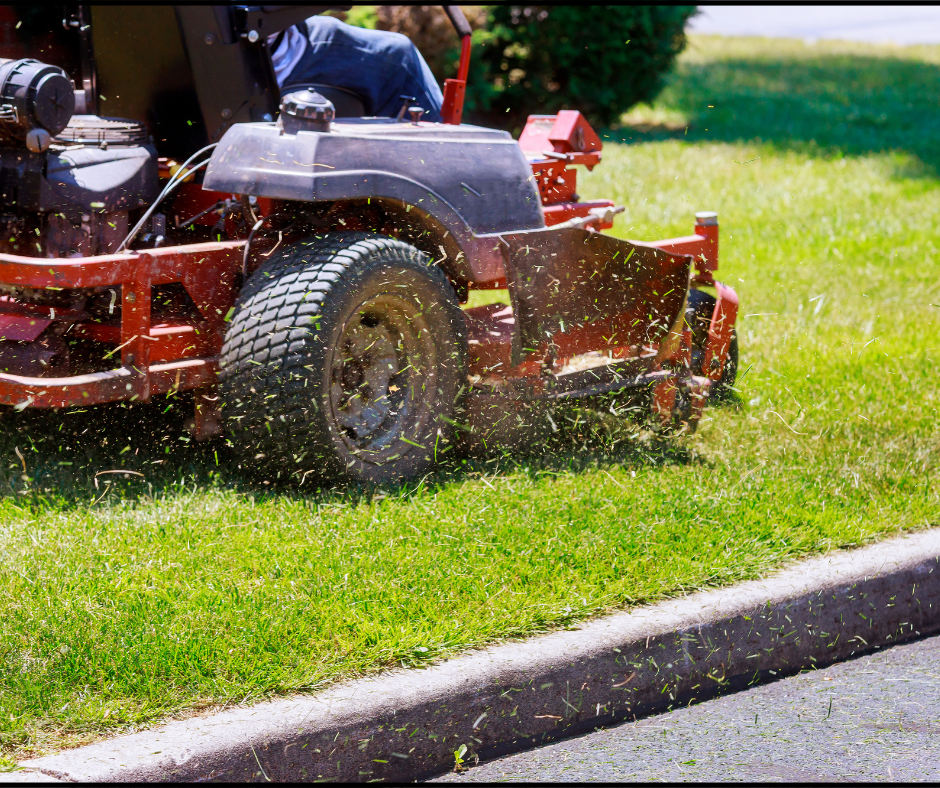 A person is riding a red lawn mower on a grassy lawn, cutting the grass and kicking up clippings.