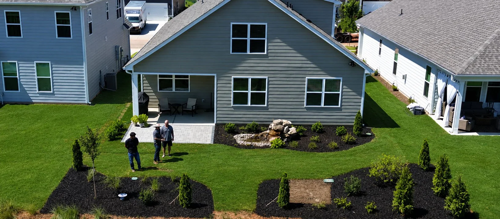 A complete backyard composition where paving, water, planting, and open lawn work together to create structure, depth, and a clear connection between the home and the landscape beyond.
