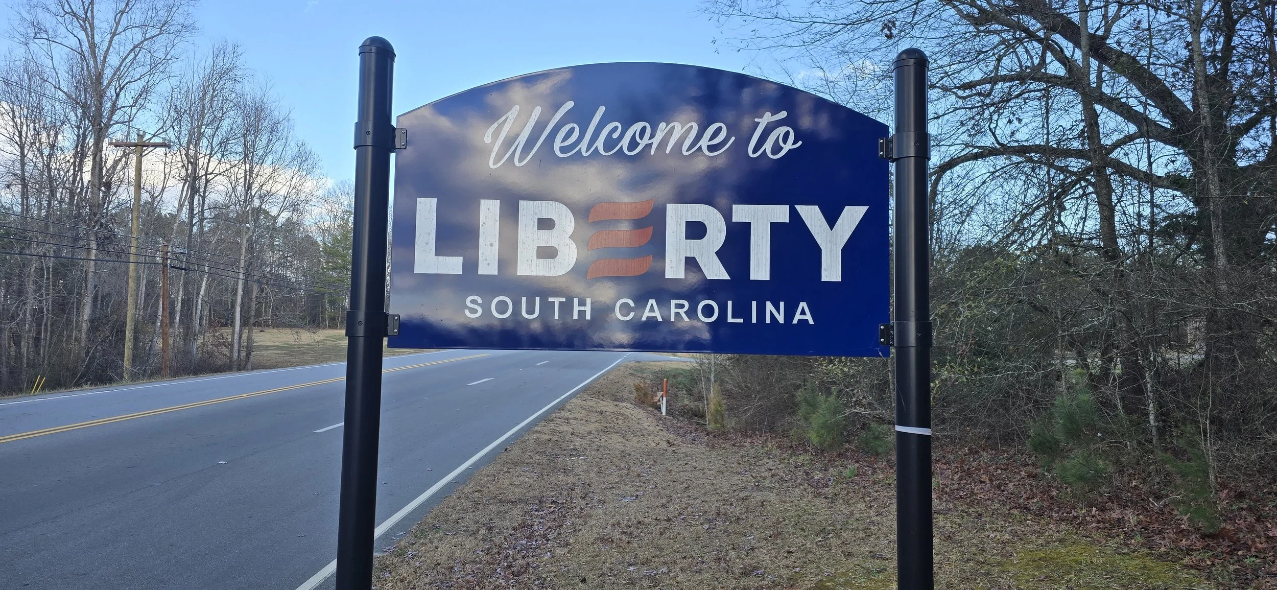 Welcome sign for Liberty, South Carolina, with blue background and white lettering, featuring a stylized American flag design in the word "Liberty."
