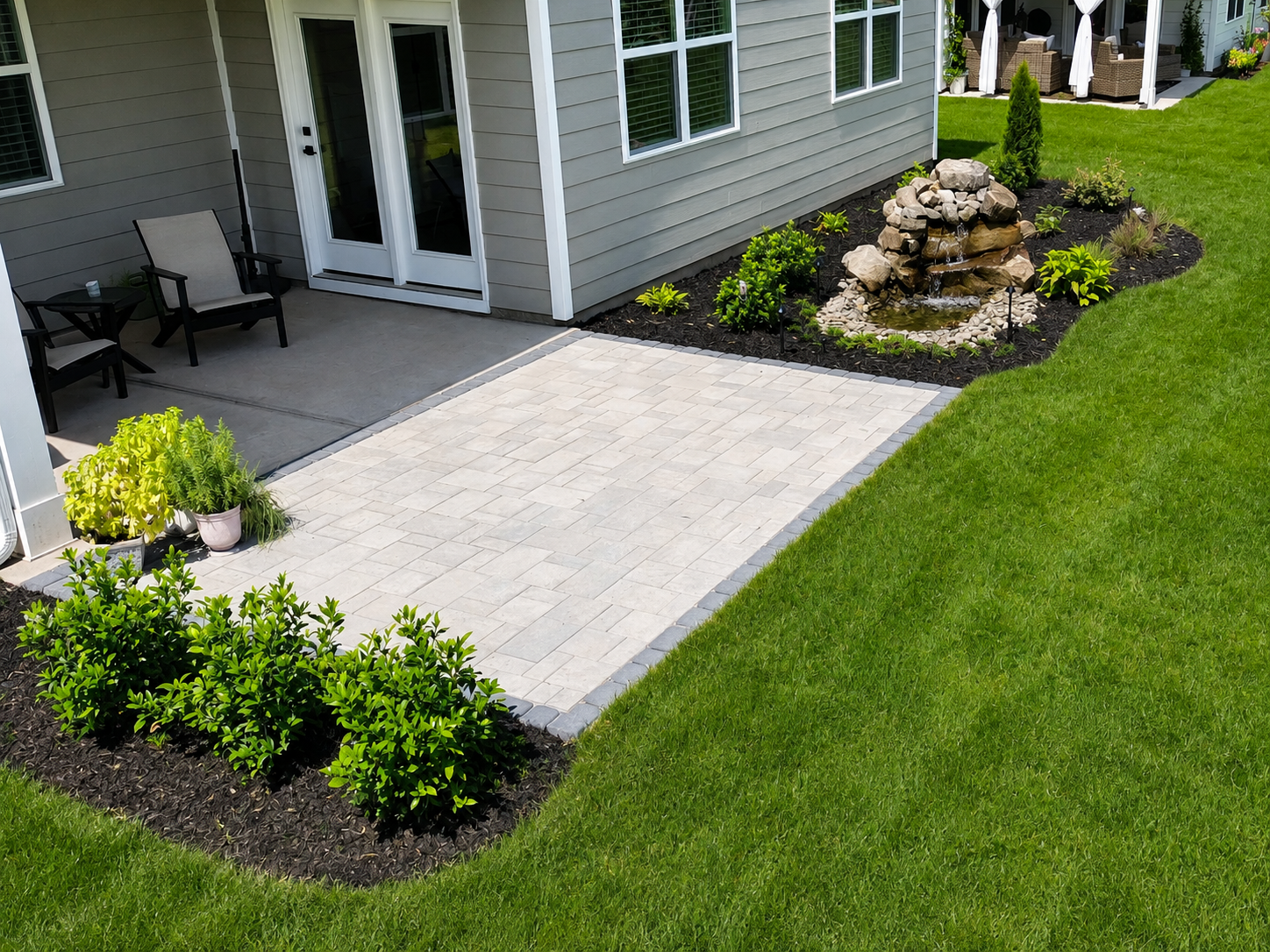 A refined paver terrace meets a custom boulder water feature, creating a backyard composition shaped by structure, movement, and natural character.