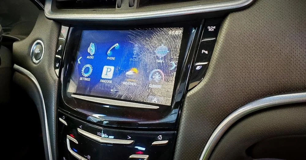 Car's infotainment touchscreen with shattered glass, displaying various app icons.