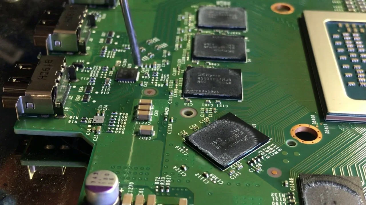 Close-up of a green computer motherboard with various black integrated circuits, connectors, and small electronic components.