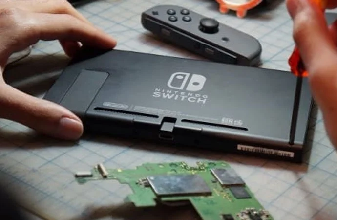 Close-up of a Nintendo Switch gaming console, a detached circuit board, and a Nintendo controller on a work table.