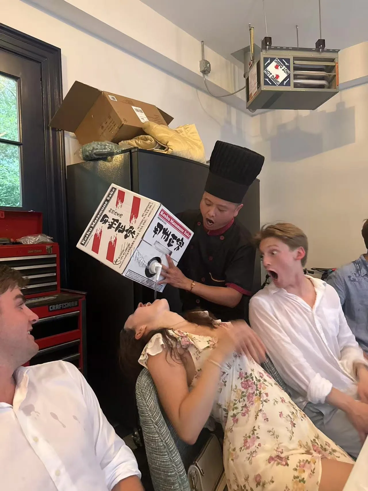 A clown holding a box over a woman and a man with shocked expressions in a restaurant or cafe setting.