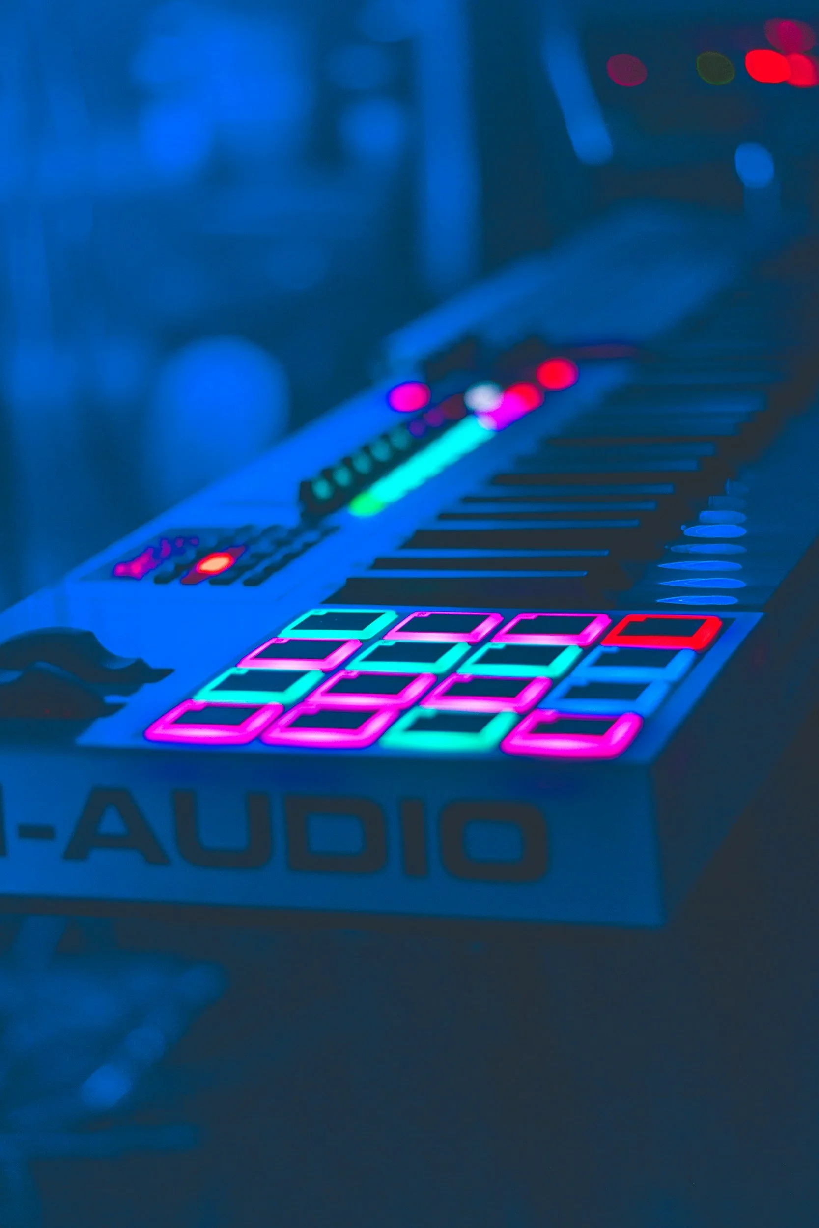 A futuristic electronic music production controller with LED-lit pads, knobs, and buttons, displayed against a dark background, used for live performance or studio production.