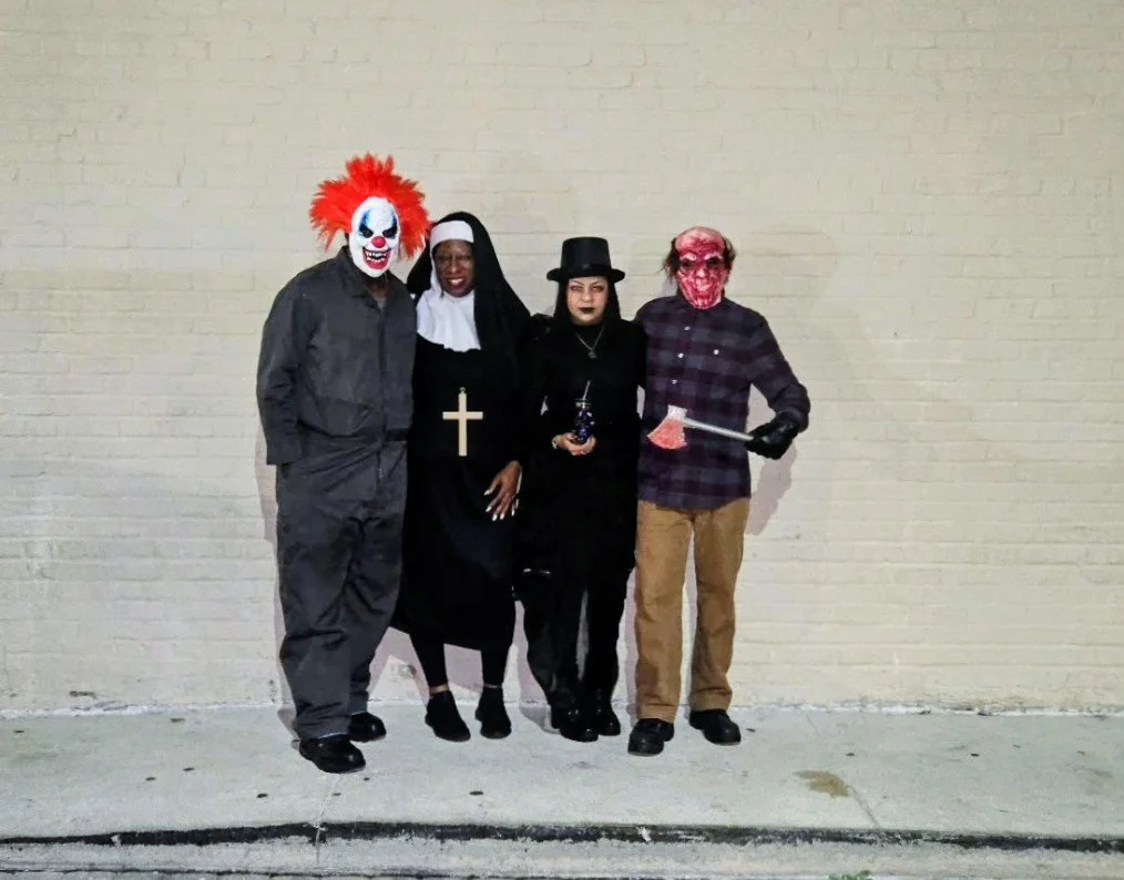 Four people dressed in Halloween costumes standing against a beige brick wall.