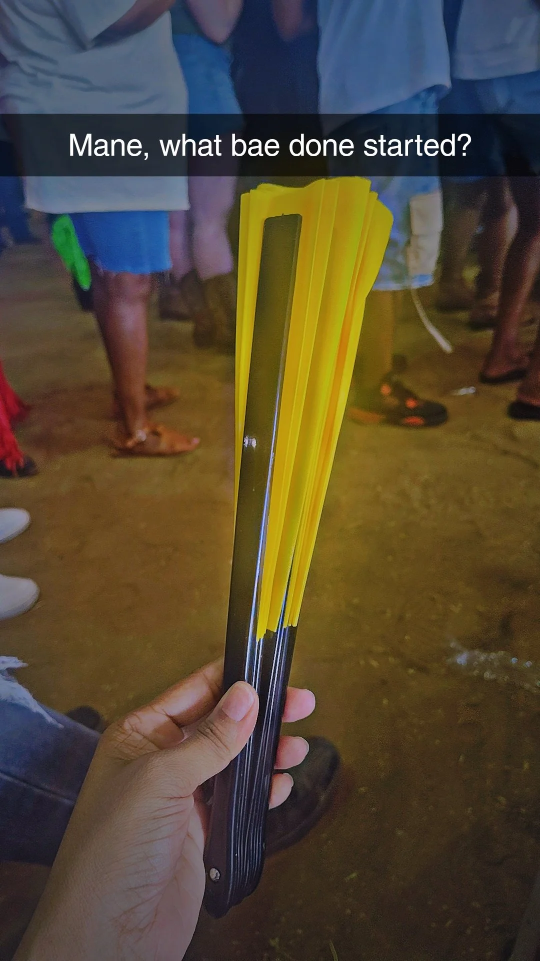 A hand holding several yellow and black lollipop sticks, with a group of people in the background.