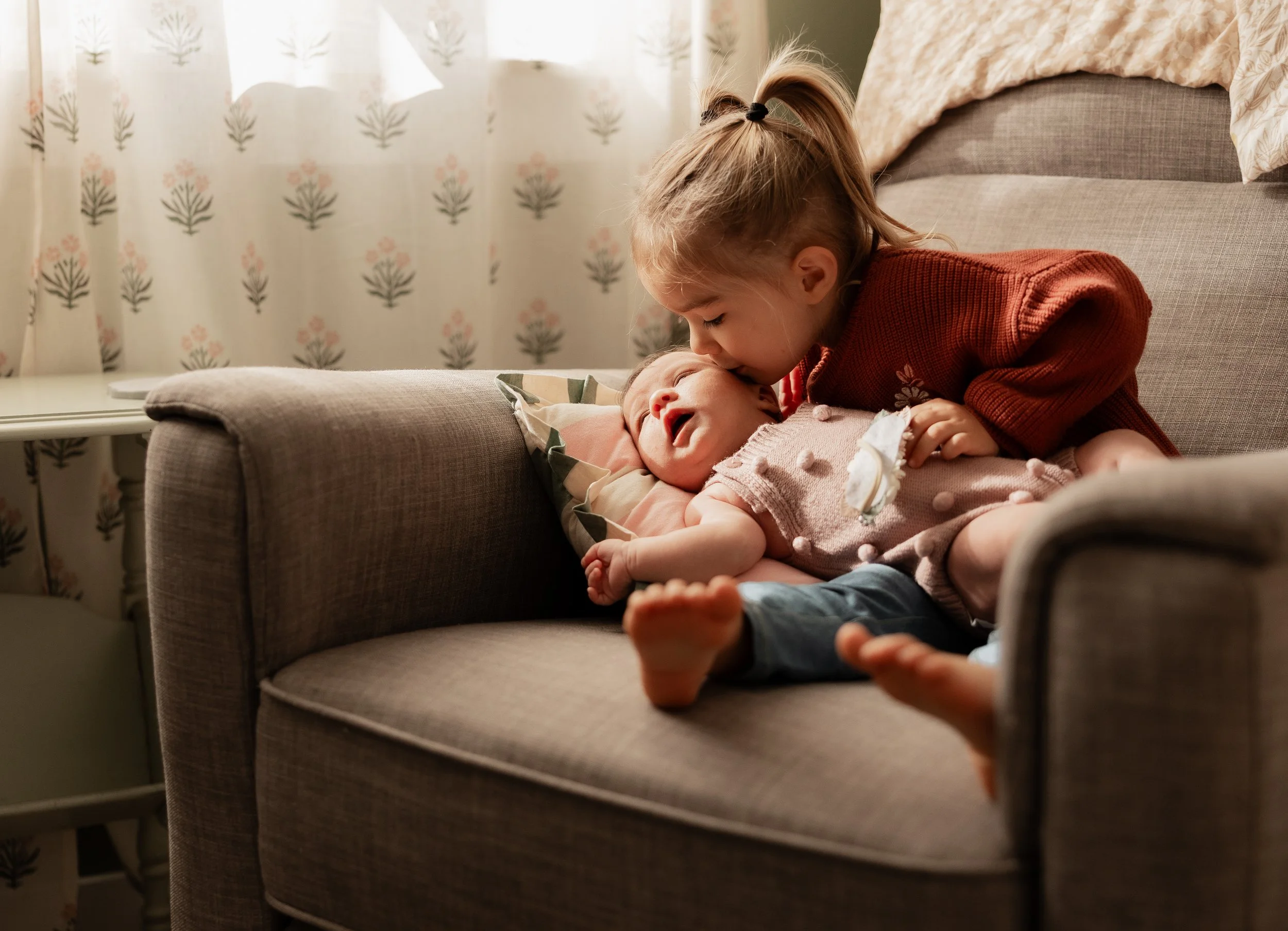 Toddler holding her newborn sister in nursery chair
