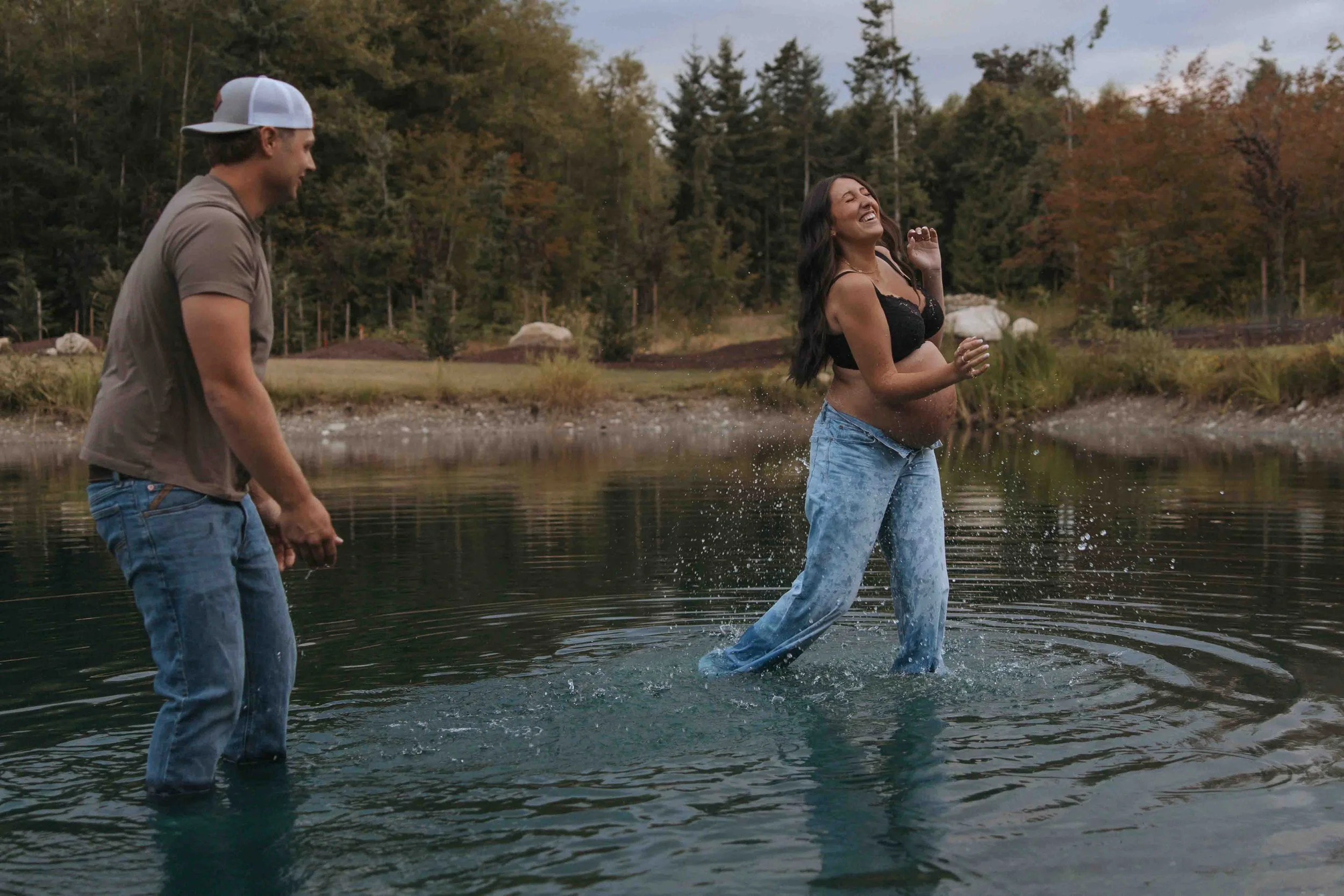 Husband and wife splashing in water during maternity photo session