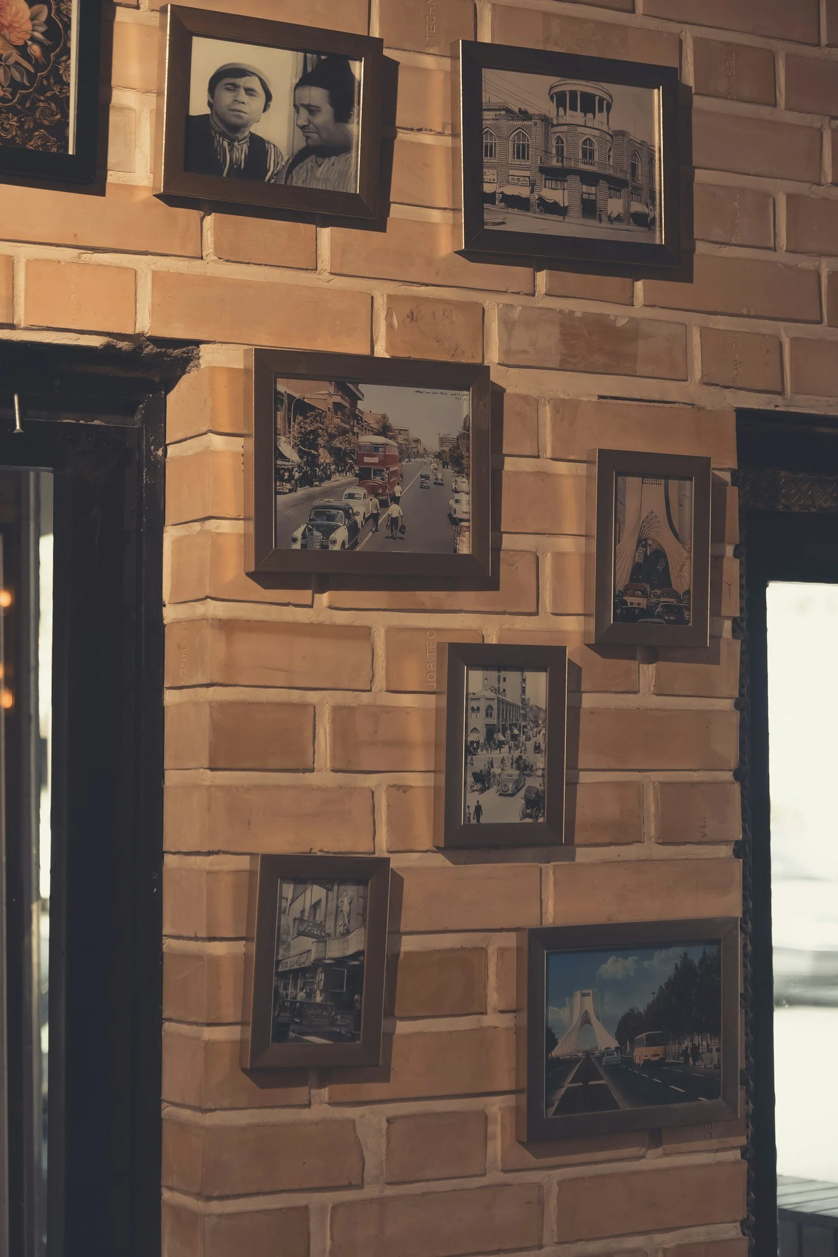 A brick wall decorated with seven framed photographs, including images of people, city streets, and famous buildings.