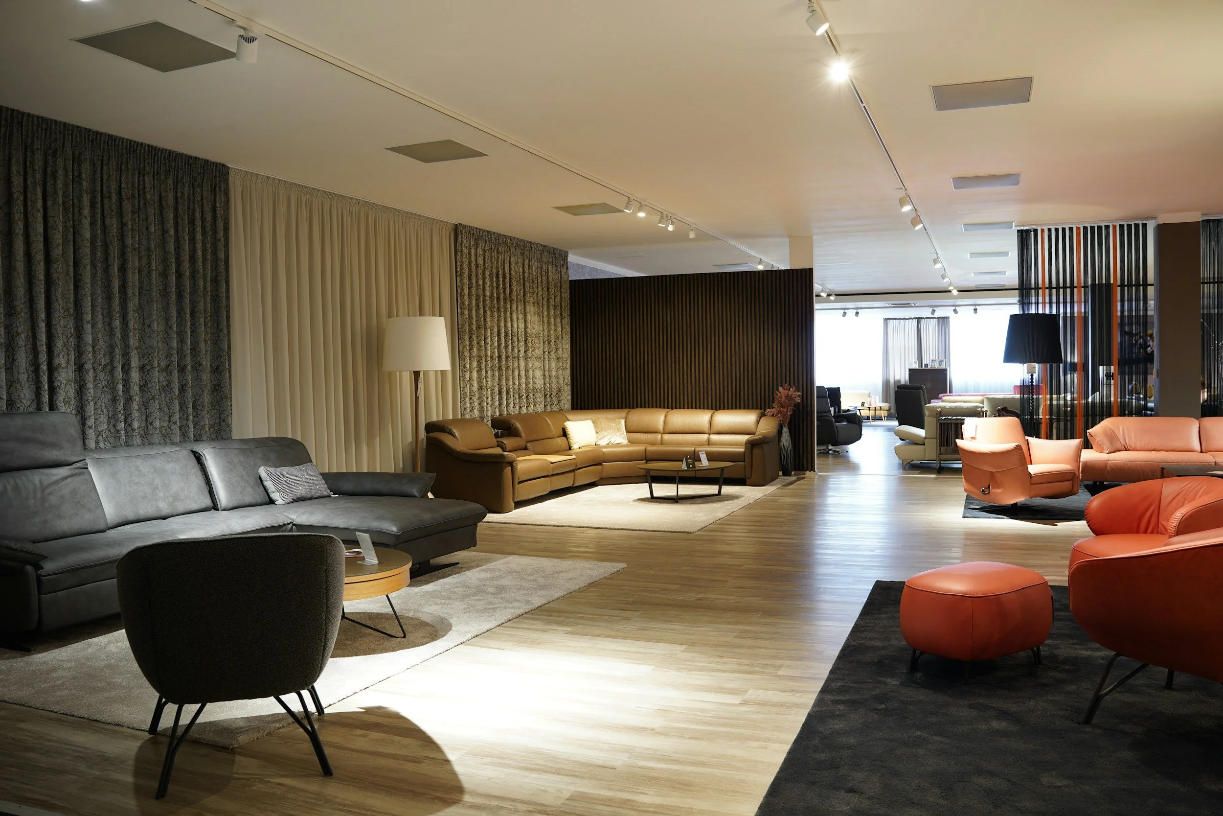 Interior of a modern lounge with various sofas, armchairs, and lighting fixtures, featuring a mix of neutral and warm tones.