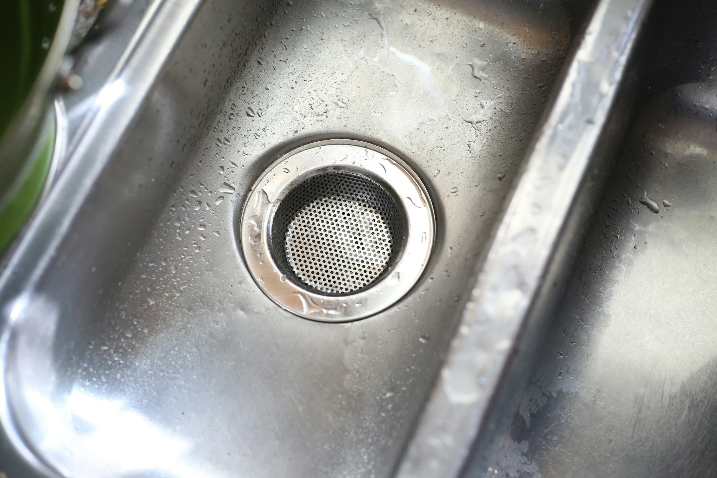 Close-up of a stainless steel kitchen sink with water droplets around the drain.