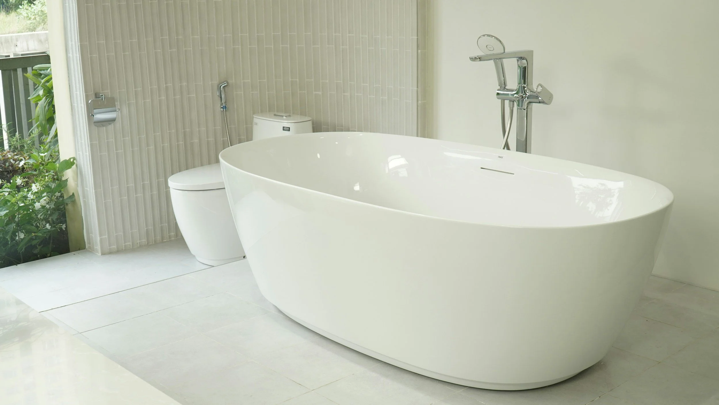 Modern bathroom featuring a freestanding bathtub, a toilet, and a garden view outside window.