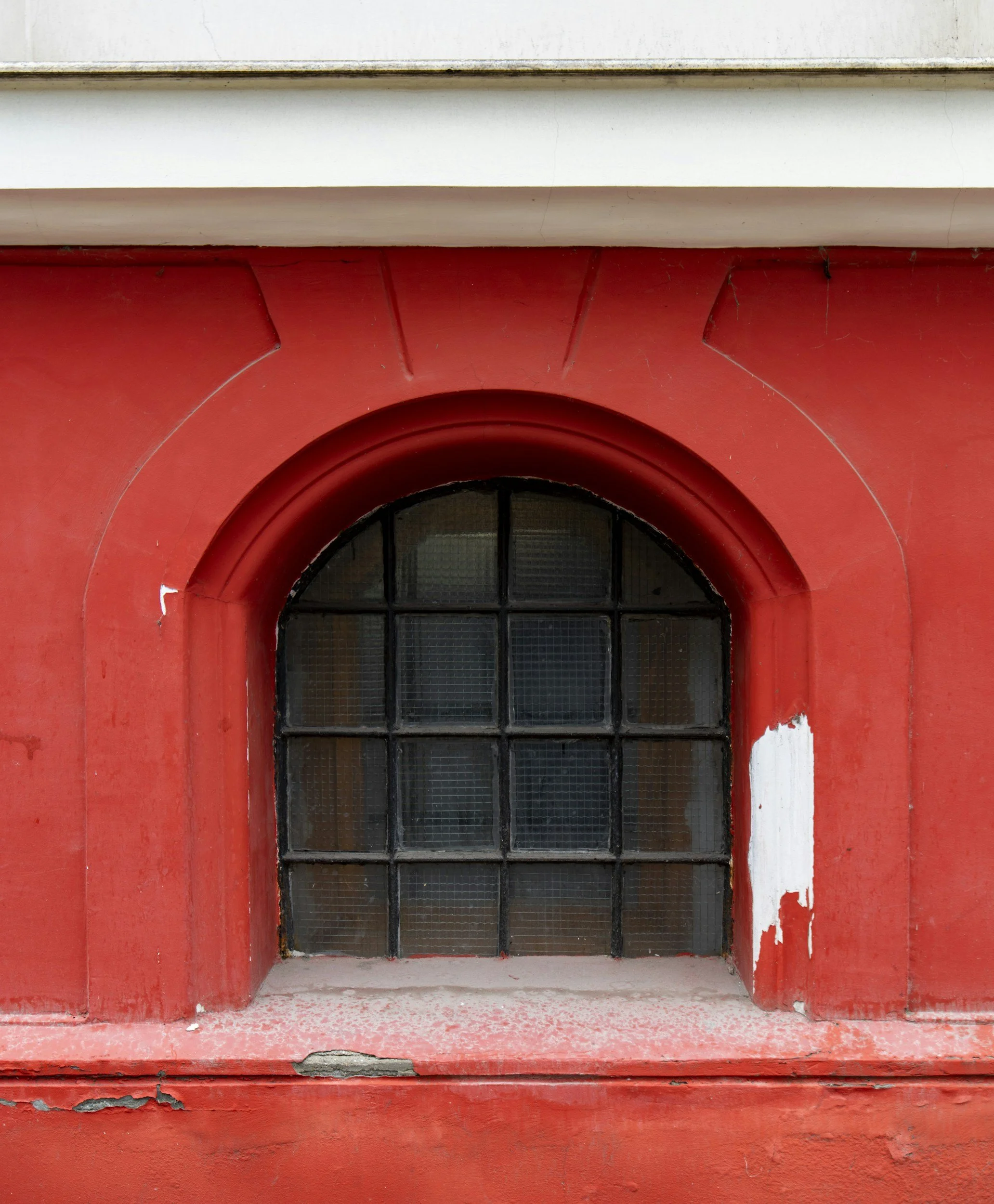 A red building exterior with a small arched glass window and peeling paint.