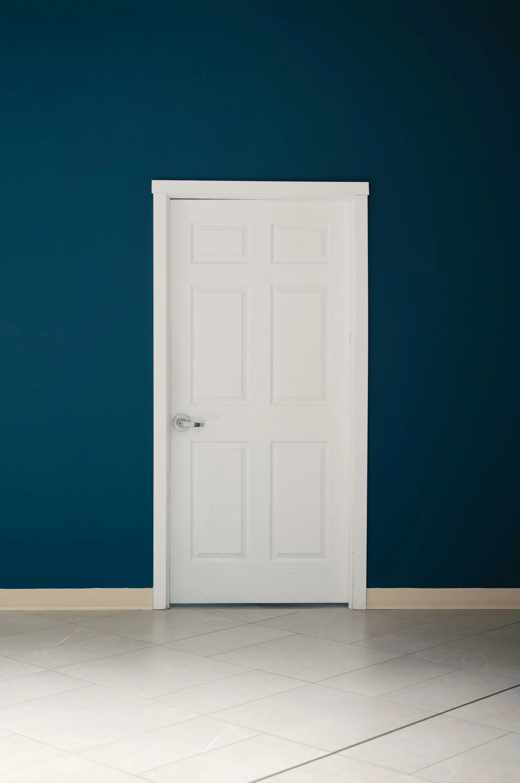 White door on a blue wall with beige tile floor.