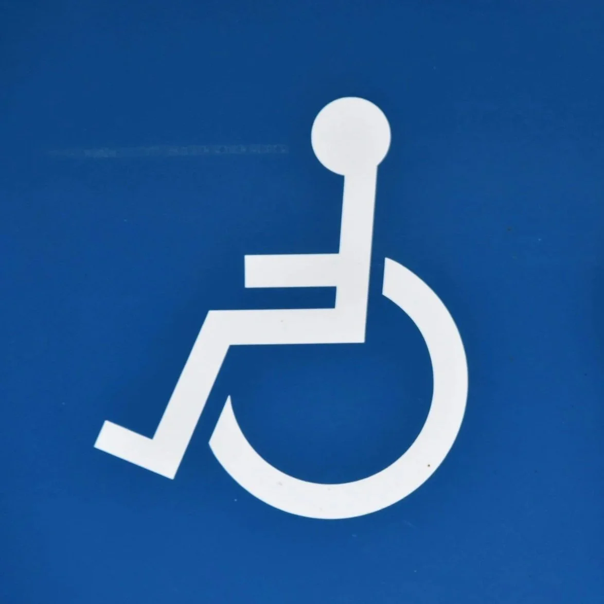 Accessibility sign featuring a white wheelchair symbol on a blue background.