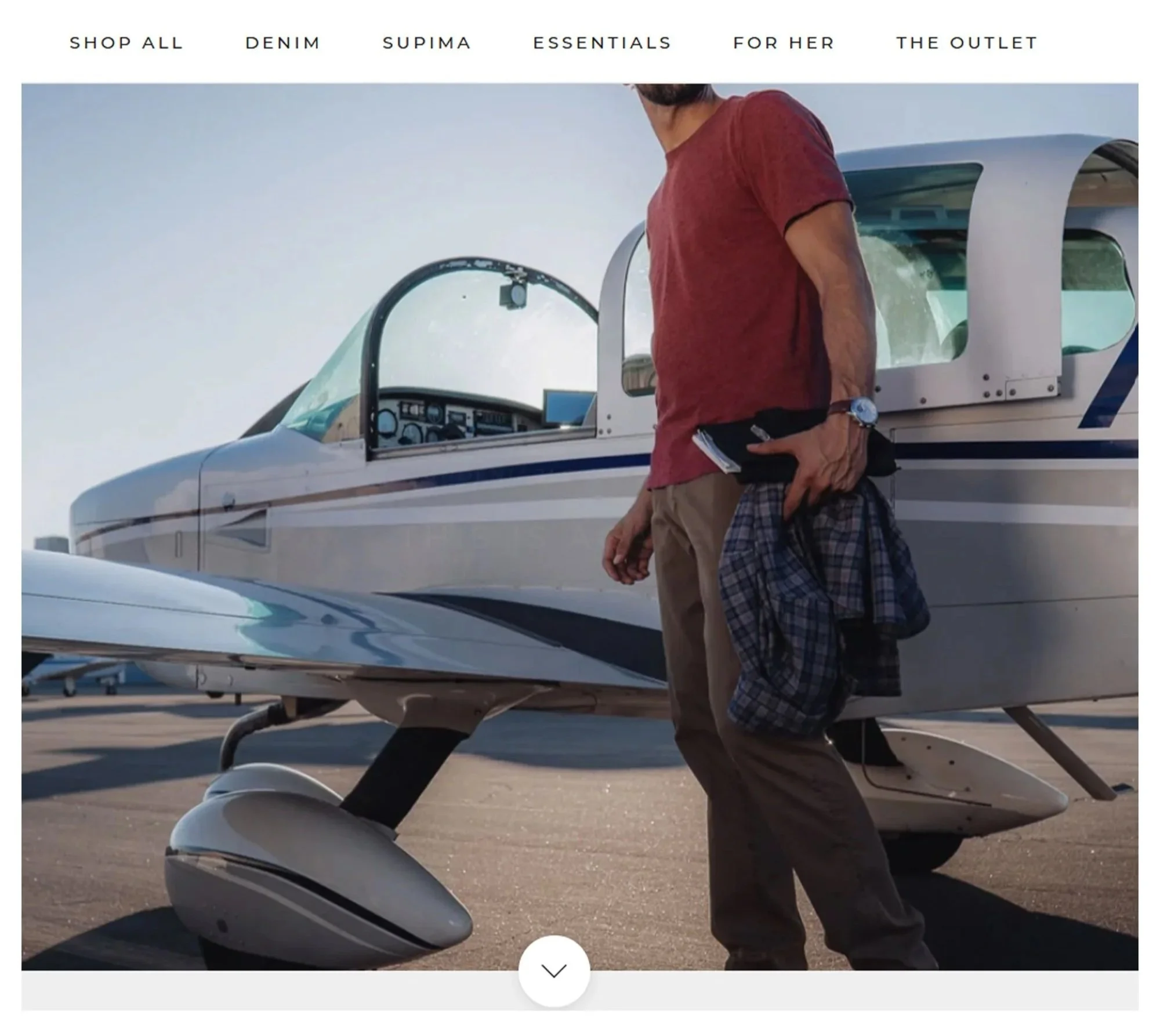 A man standing next to a small private airplane, holding a plaid jacket and notebook, on a tarmac at sunset.
