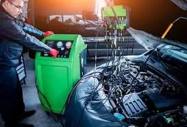 A person using a green industrial tool on a car engine in a garage