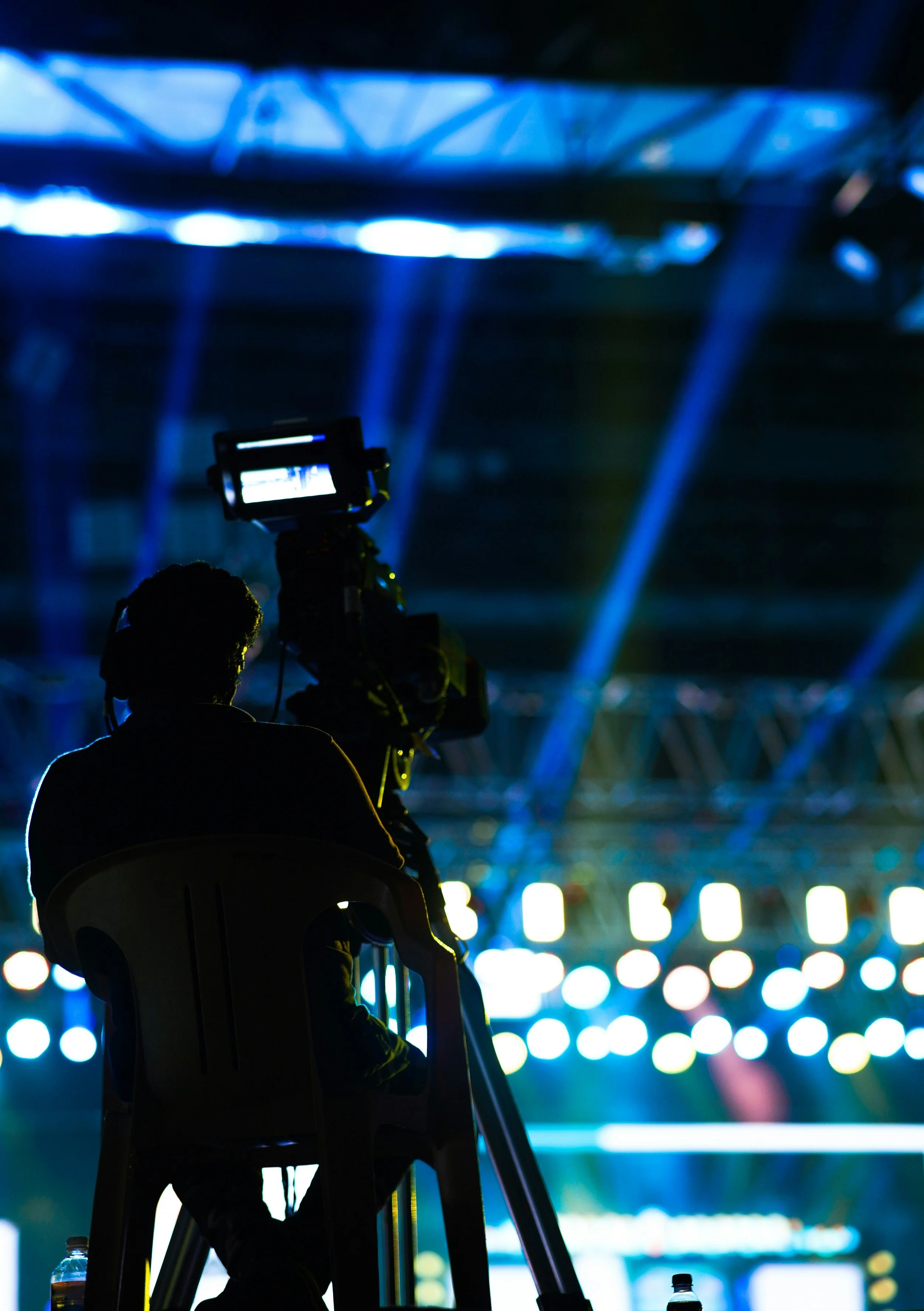 A silhouette of a person sitting on a chair and taking a photo with a camera at nighttime, with colorful illuminated lights in the background.