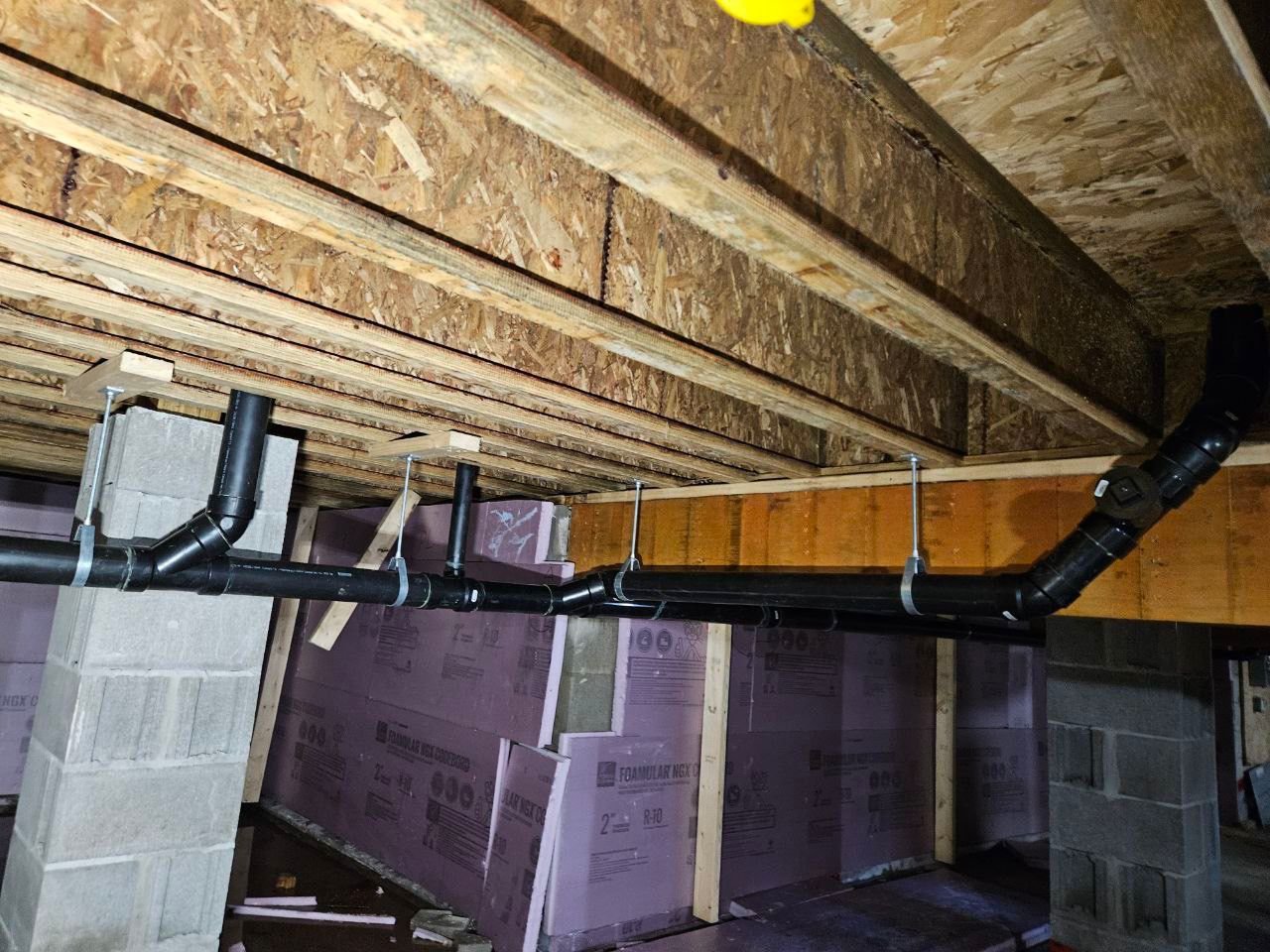 Drain pipe installation under joists in basement crawl space.