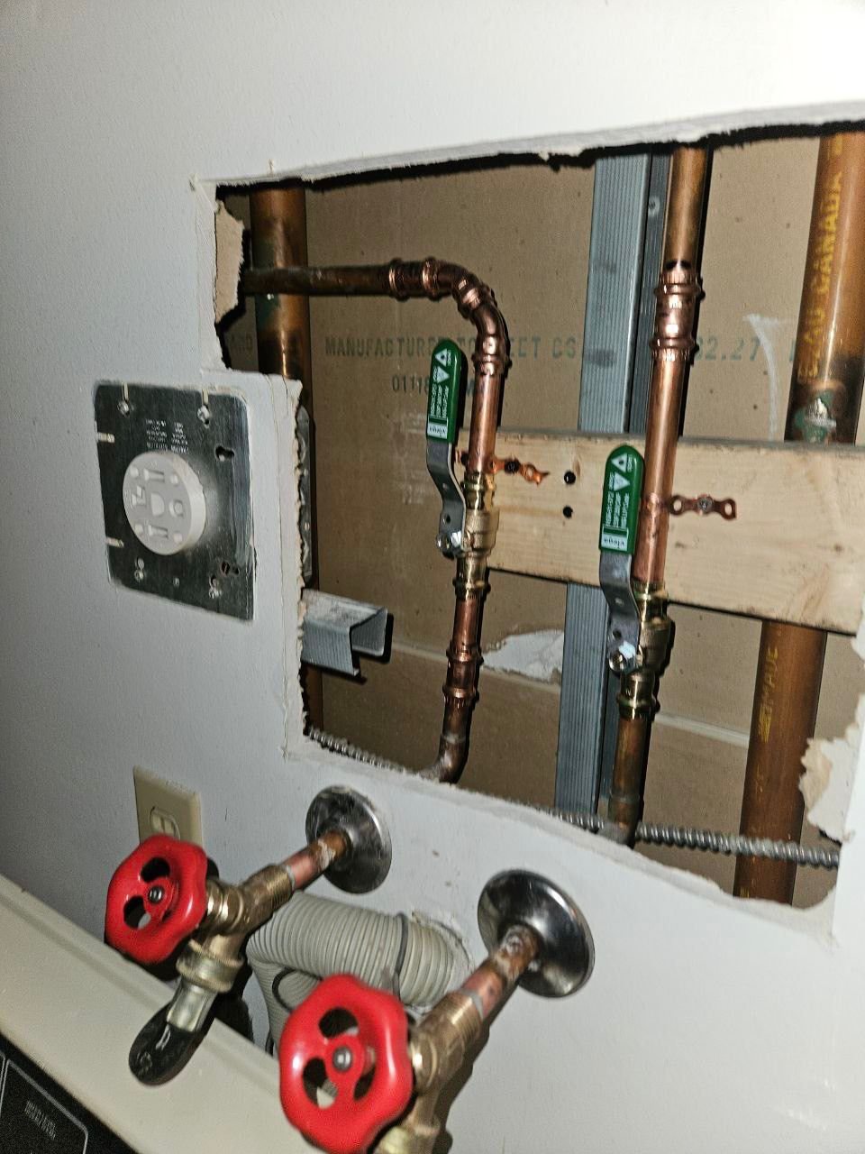 Copper water supply pipes with red-handled shutoff valves for laundry appliances