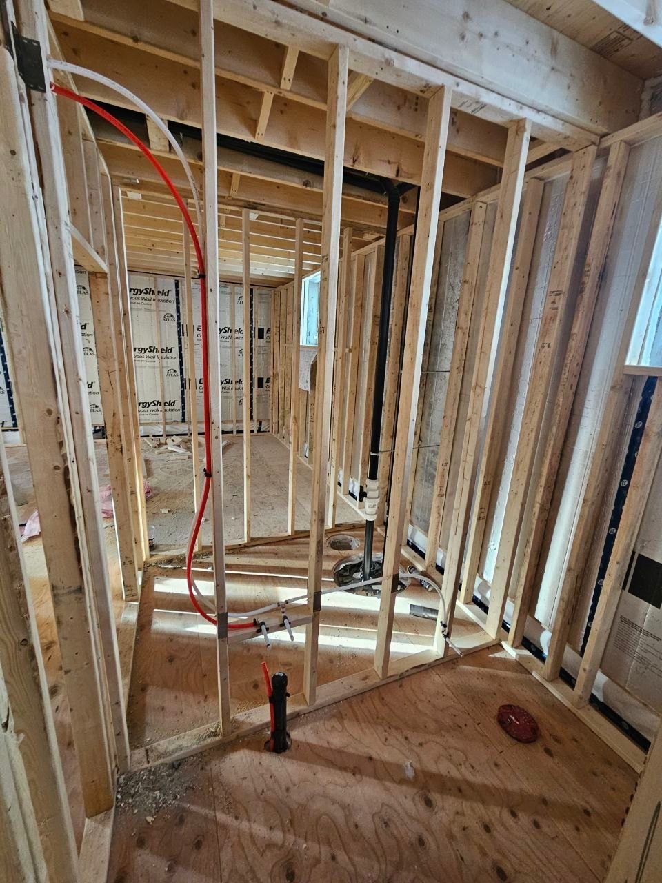 Framed wall with red and white PEX pipes and black drain pipes for bathroom plumbing