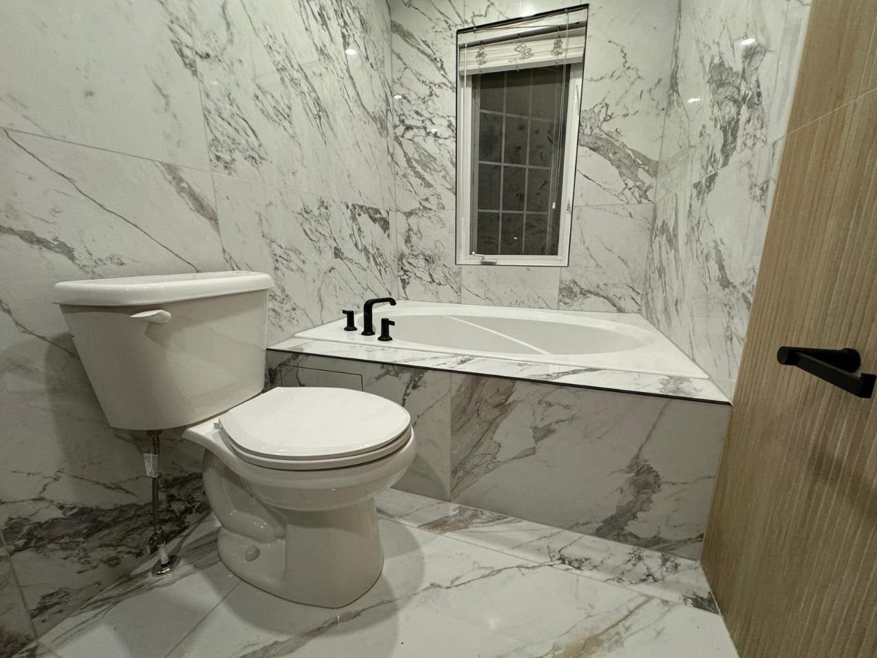 Bathtub and toilet installed with full-height marble-look tile walls, creating a clean, luxurious bathroom finish
