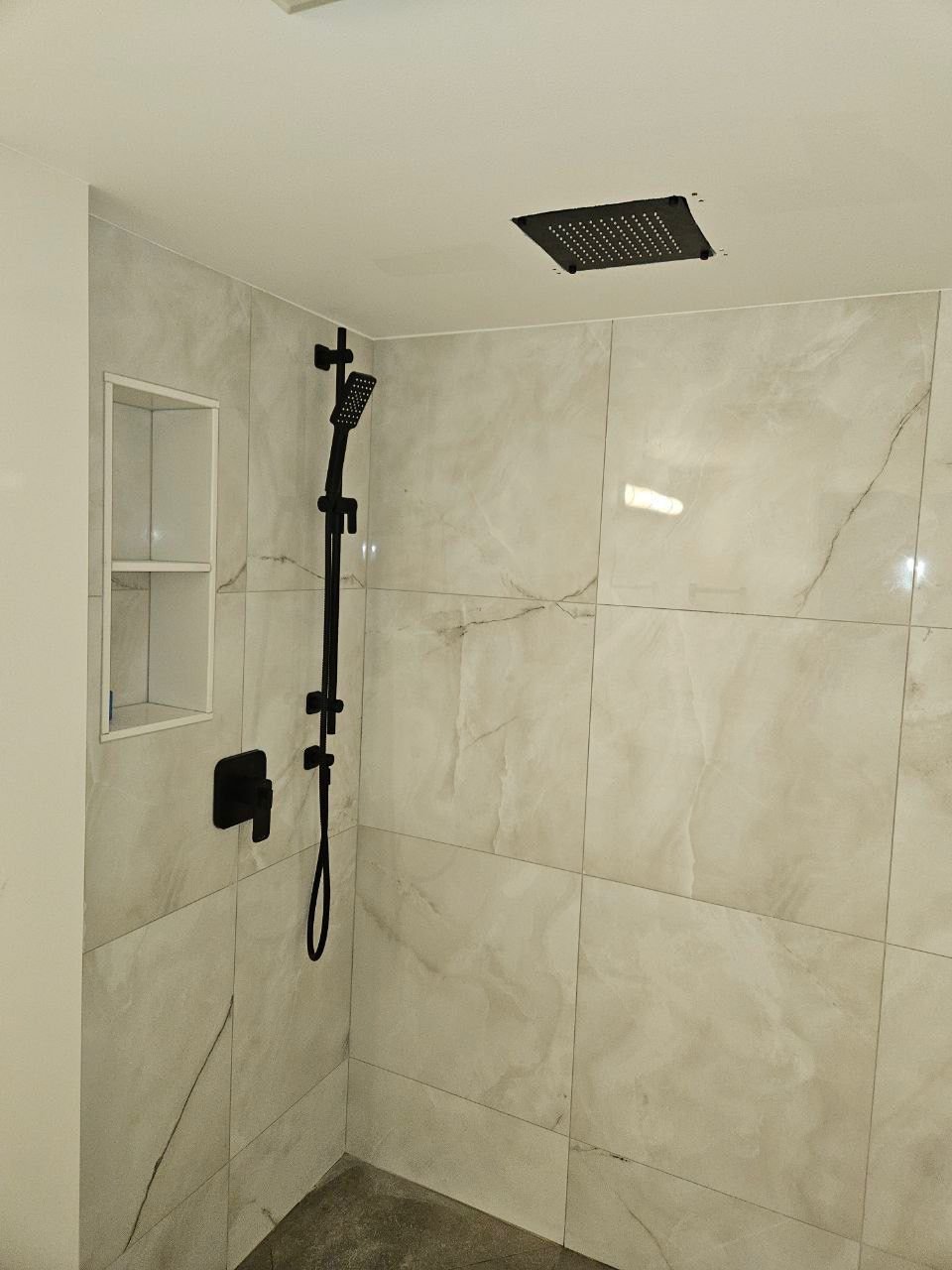 Finished walk-in shower with large porcelain tiles and matte black fixtures.