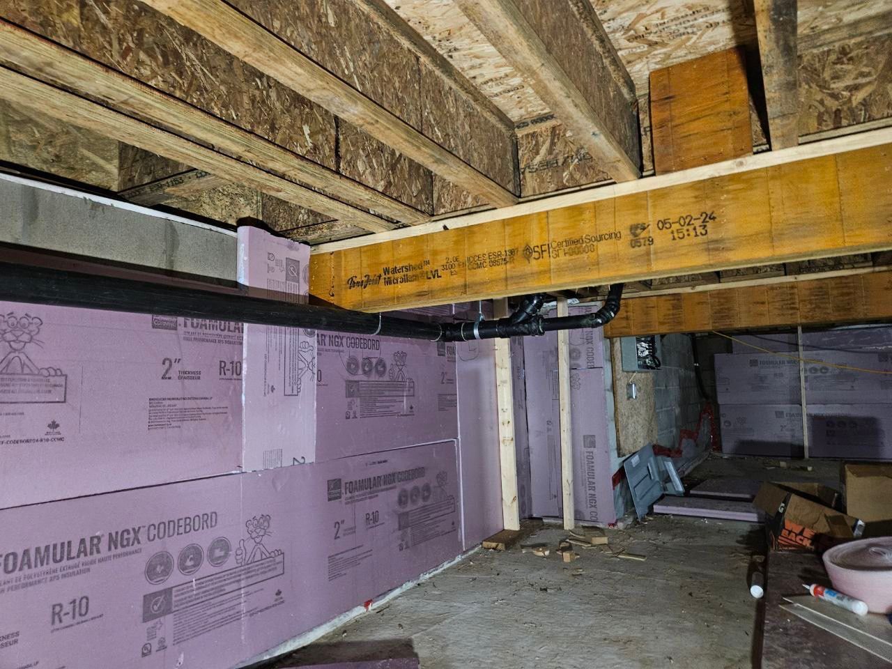 Suspended black plastic drain pipes installed along basement ceiling and walls.