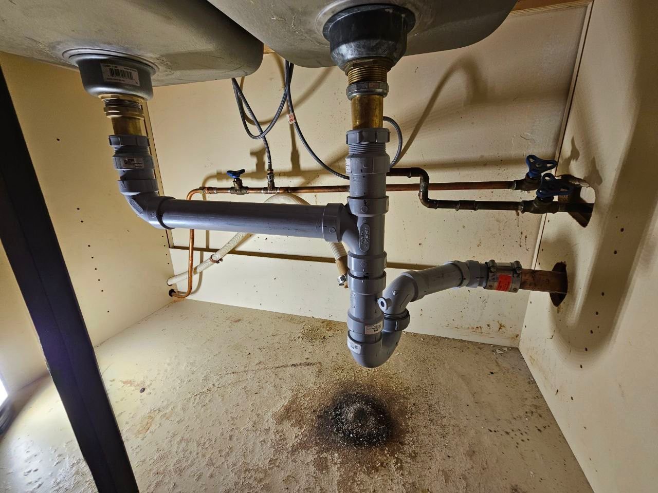 Old under-sink plumbing with PVC drain pipes and copper water lines